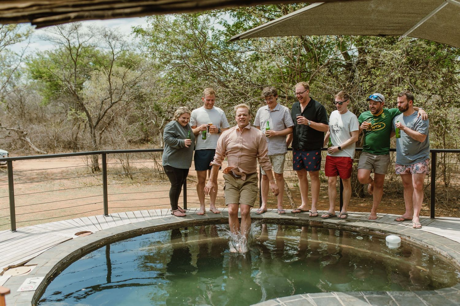 People standing around the edge of a natural swimming pool surrounded by trees and rocks.