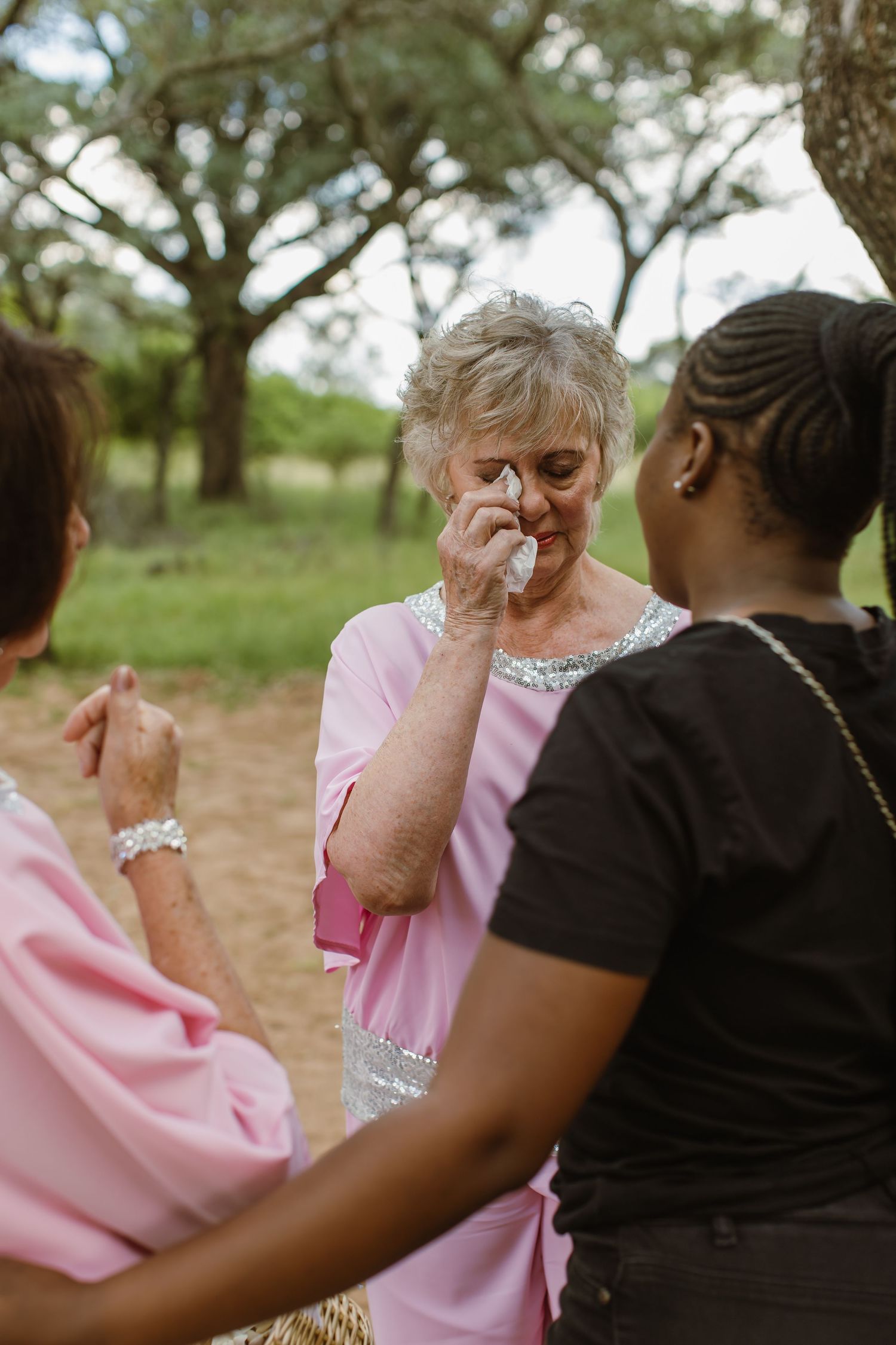 Emotional wedding guests comfort each other during an outdoor ceremony.