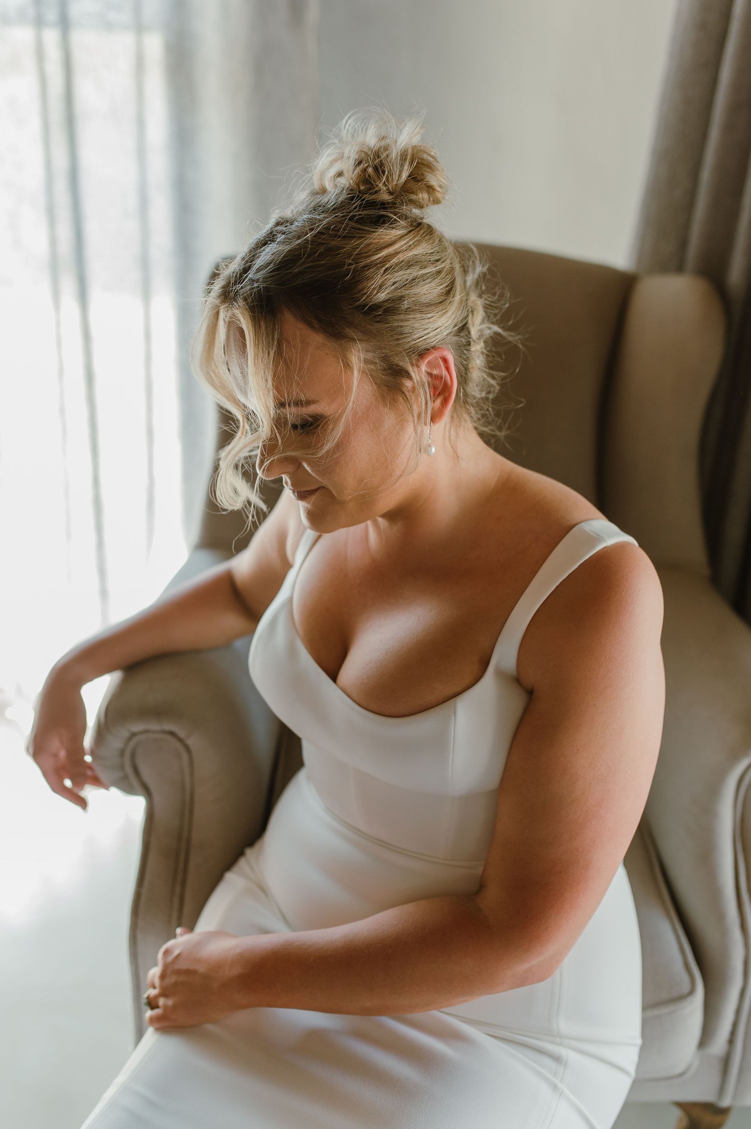 A person in white clothing sits in a gray armchair by a window.