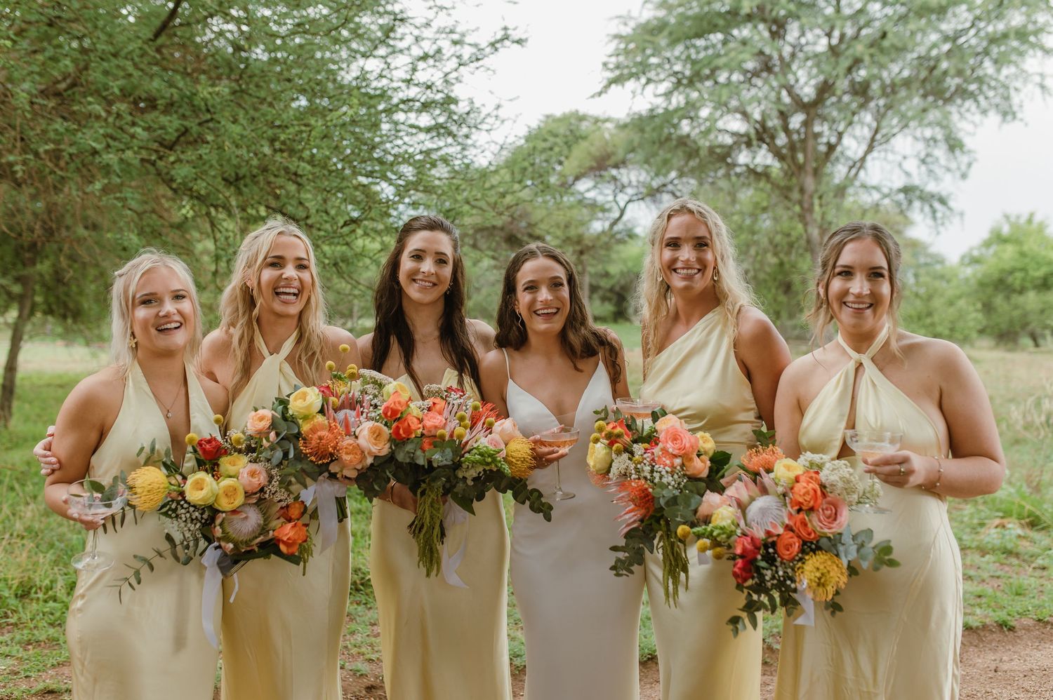 Wedding party lineup outdoors with bridesmaids holding vibrant orange and yellow bouquets.