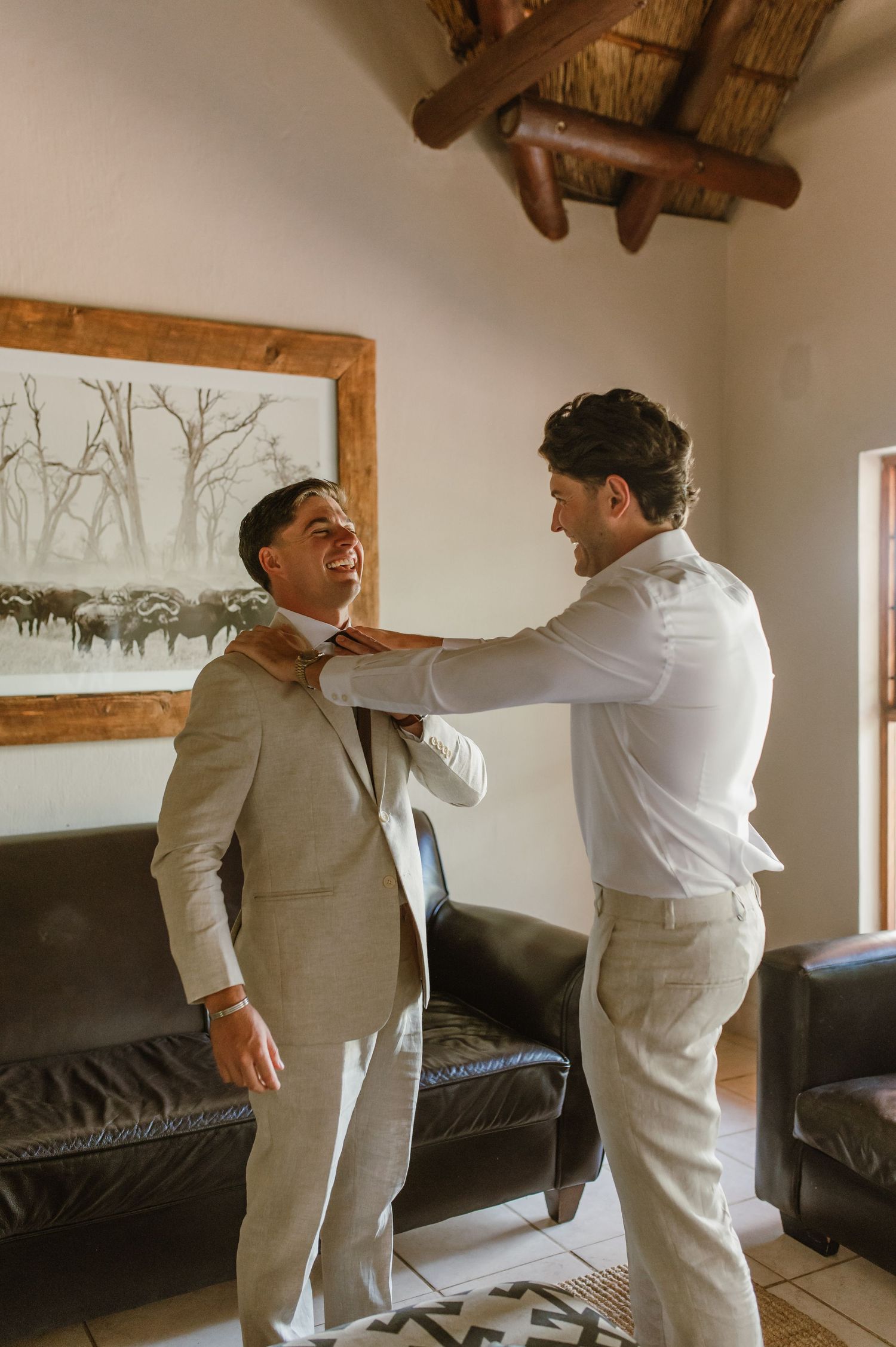 Two people in formal wear helping each other get ready in a room with rustic decor.