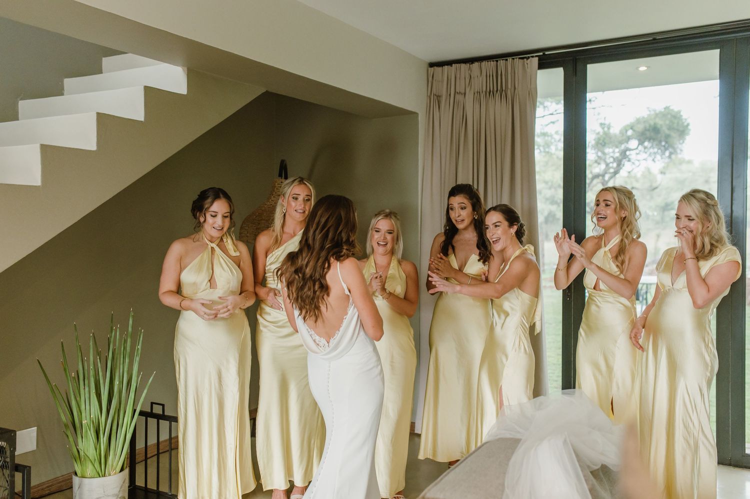 Several people in cream-colored dresses pose together in an architectural interior space.