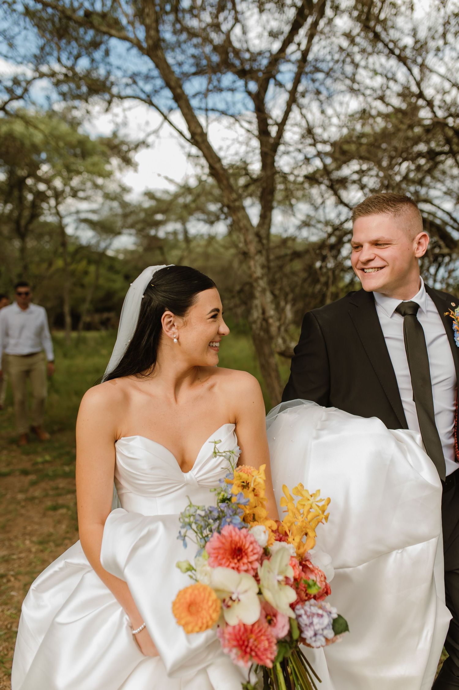 Smiling bride and groom walking together outdoors, bride holding a colorful bridal bouquet after ceremony.
