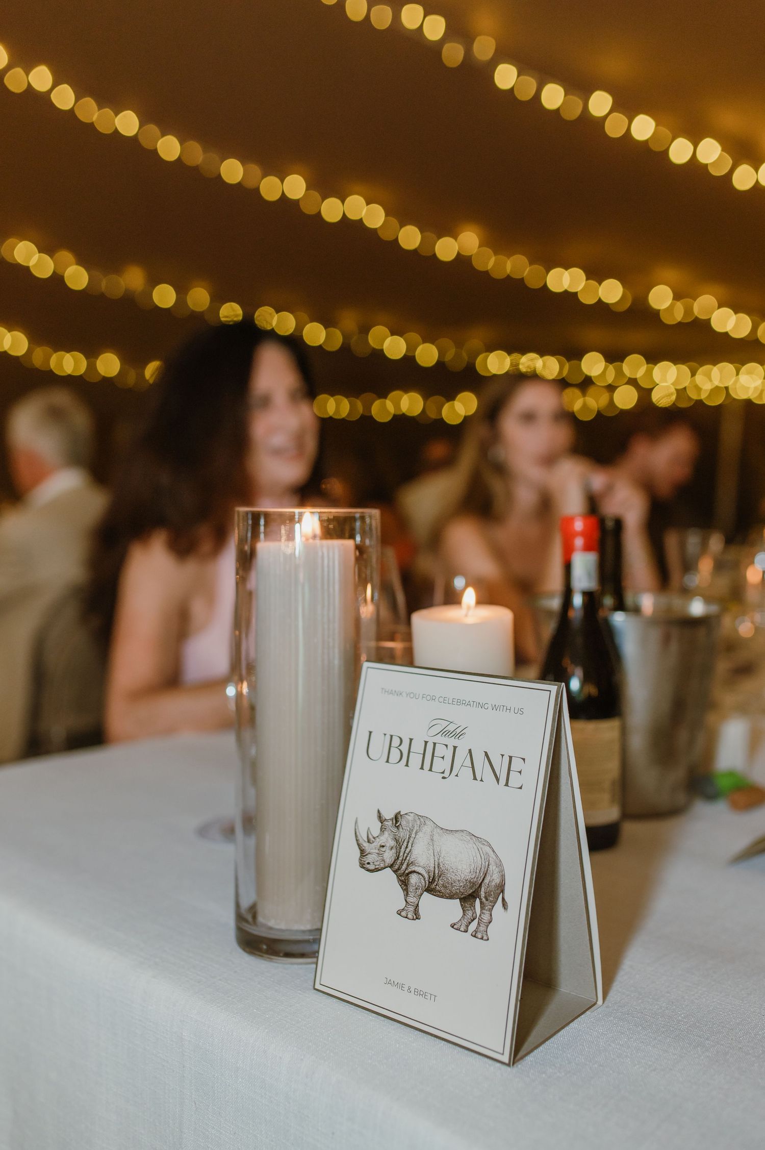 Wedding table decor with candle and Ubhejane table number card under twinkling lights.
