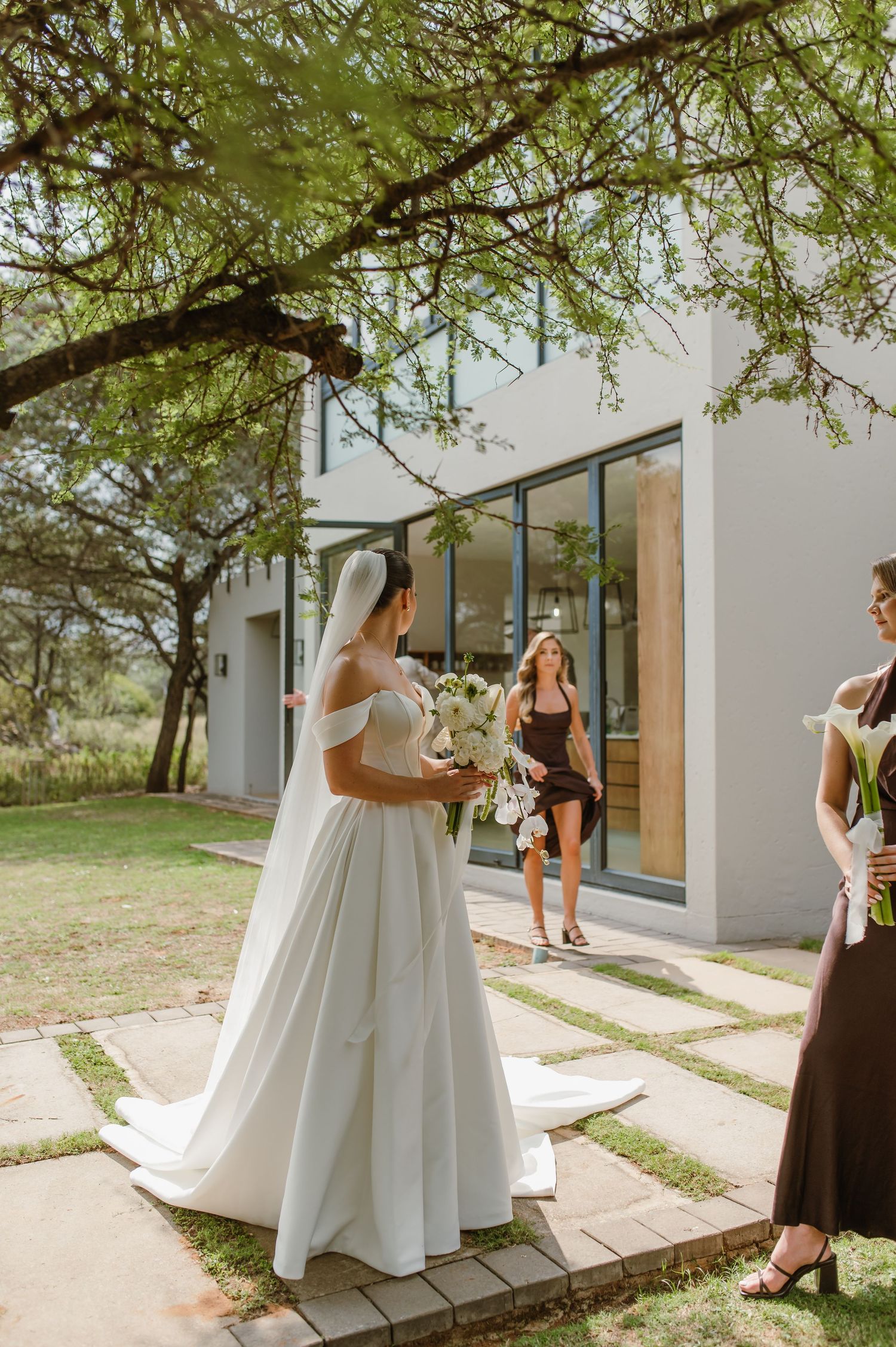 Wedding scene on modern patio with bride and attendants under tree branches.