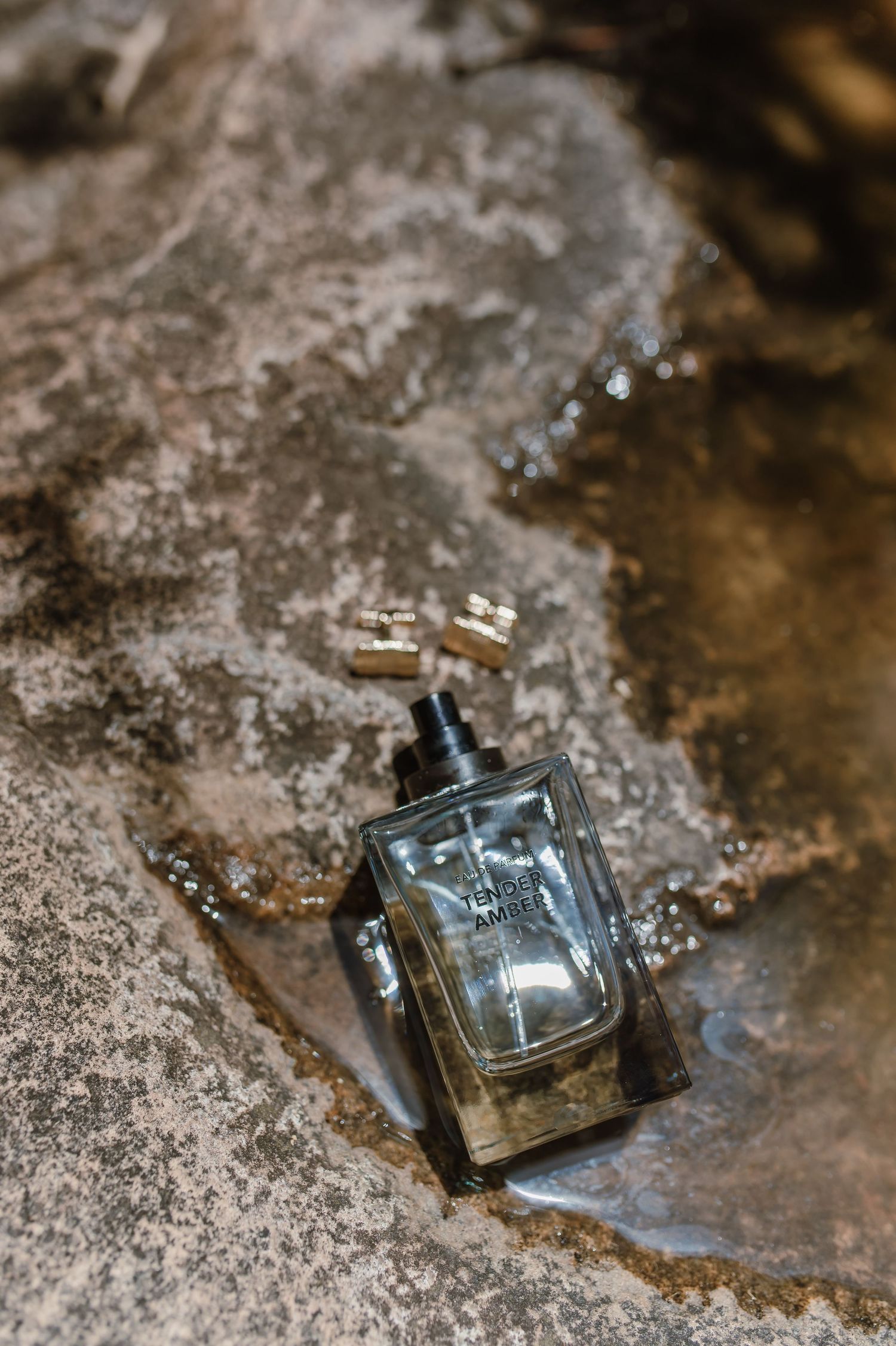 Glass perfume bottle displayed on textured stone surface with natural lighting.