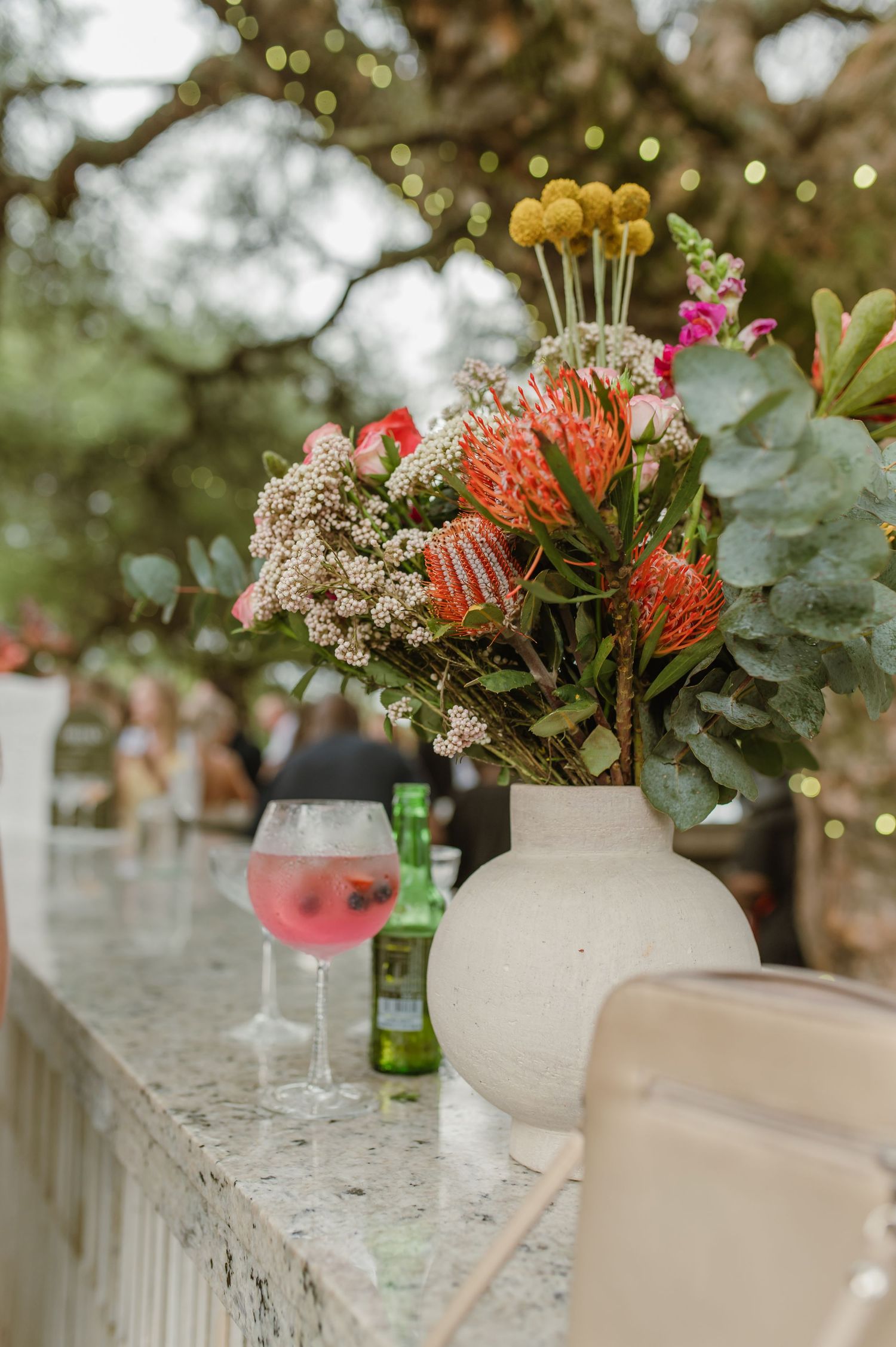 Elegant floral arrangements with protea flowers and greenery on white tables.