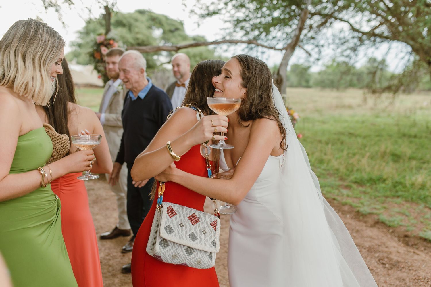 Bridesmaids in coral and green dresses celebrate at an outdoor wedding.