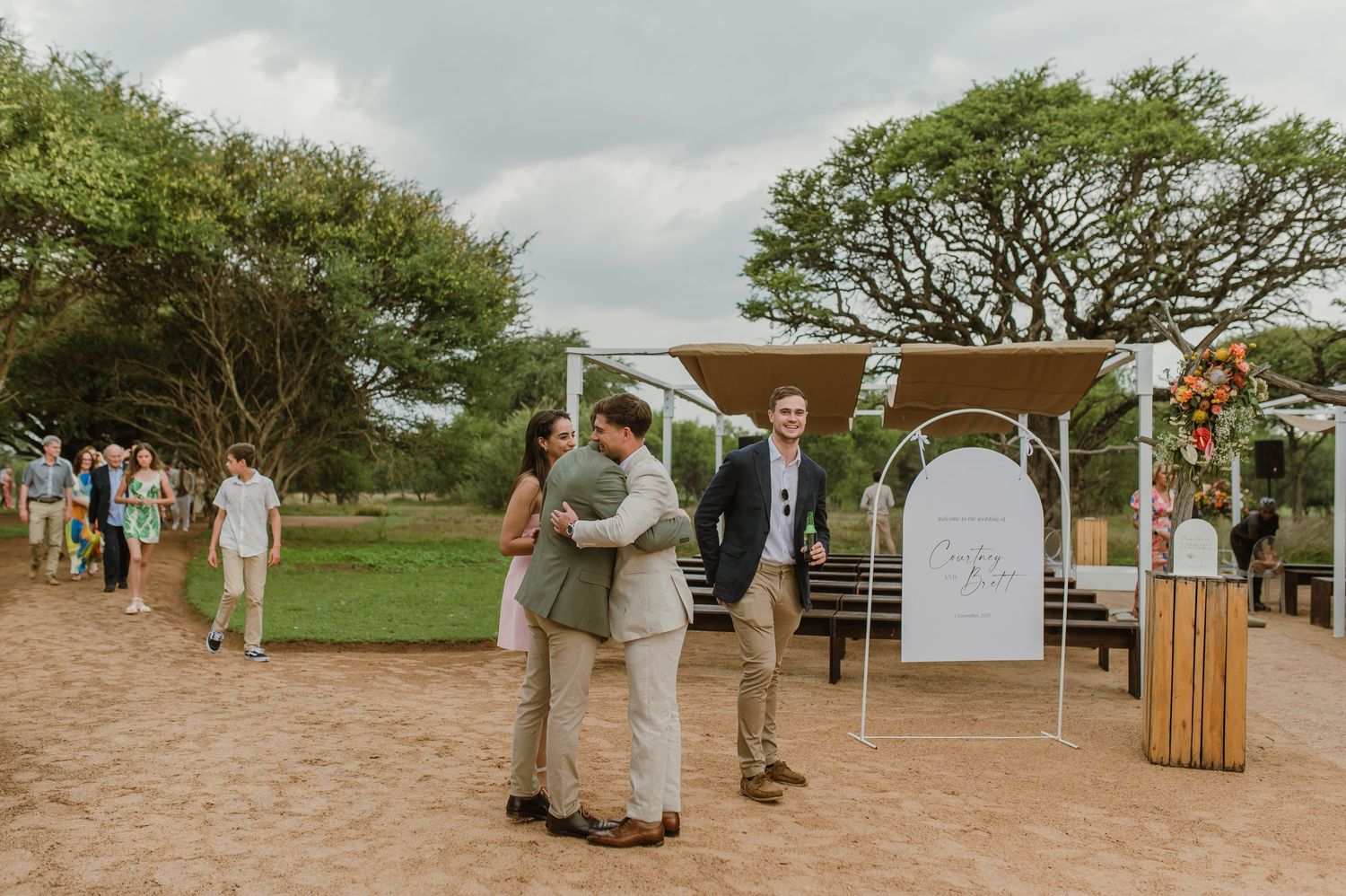 Wedding guests gather at a rustic outdoor ceremony venue with wooden seating and natural surroundings.