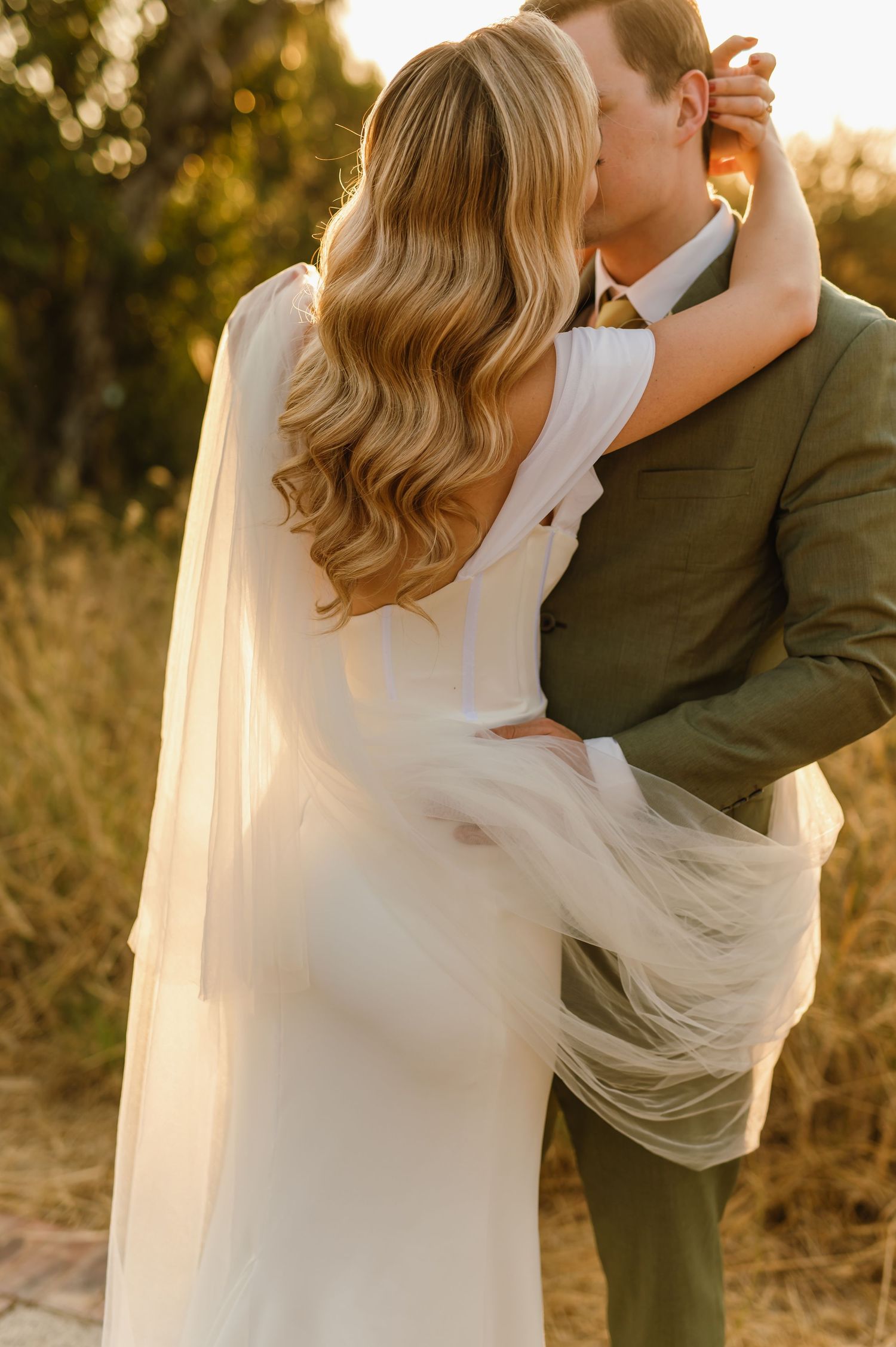 Elegant wedding couple shares a tender moment as sunlight filters through a flowing veil.