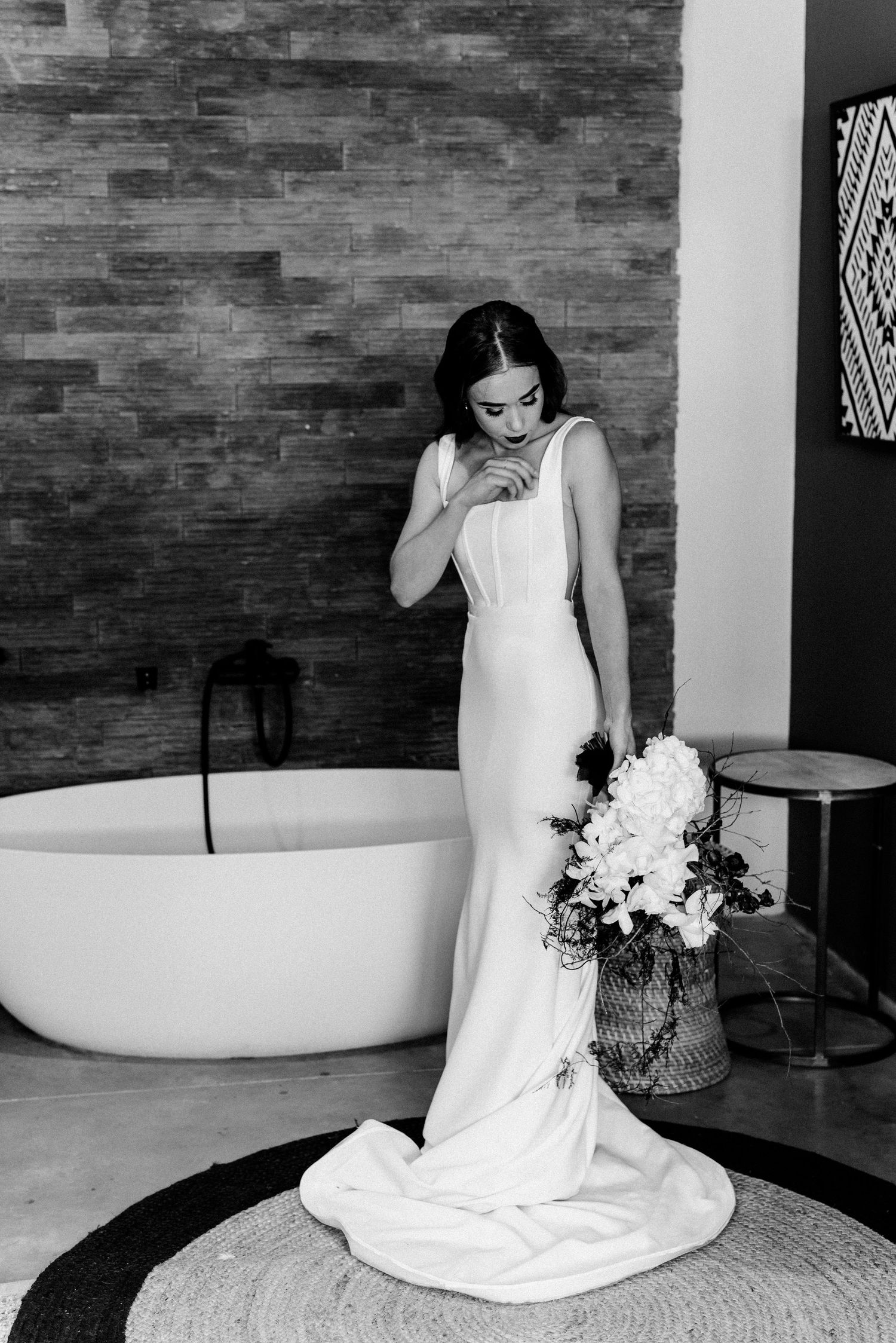 Black and white bridal portraits on a round woven rug with stone wall background.