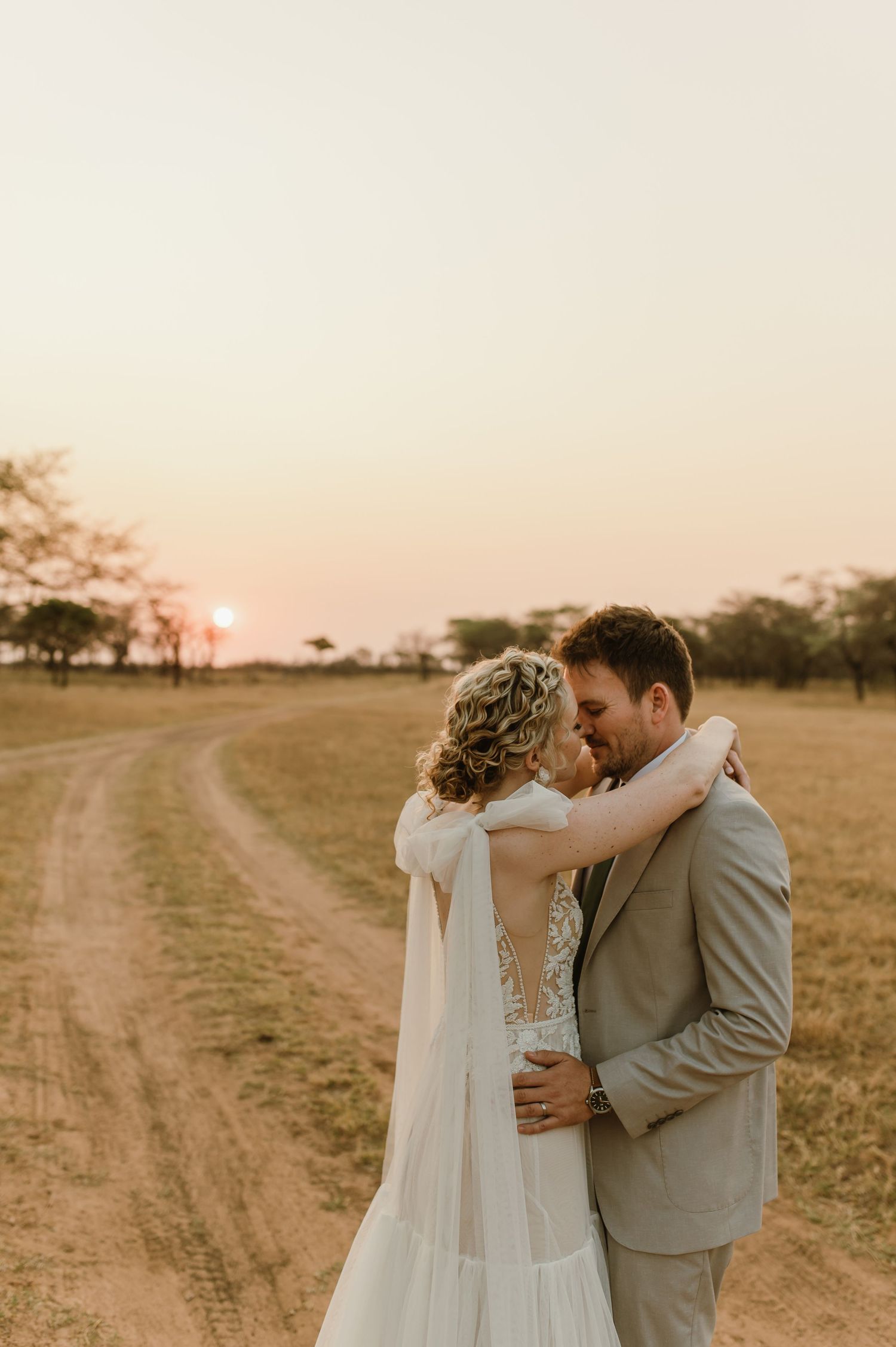 Romantic sunset wedding portraits on dirt road with acacia trees in background.