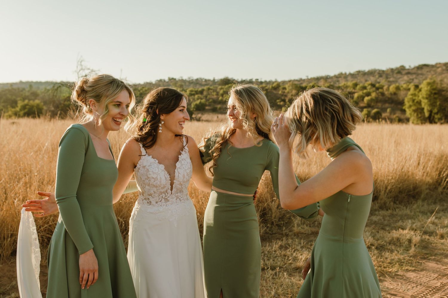Wedding party poses together in a field with rolling hills and golden light.