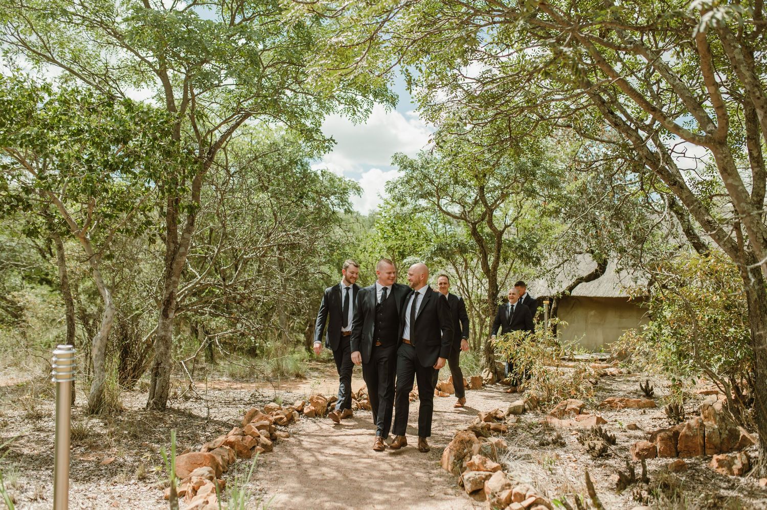 Wedding party walking through a scenic garden path lined with trees.