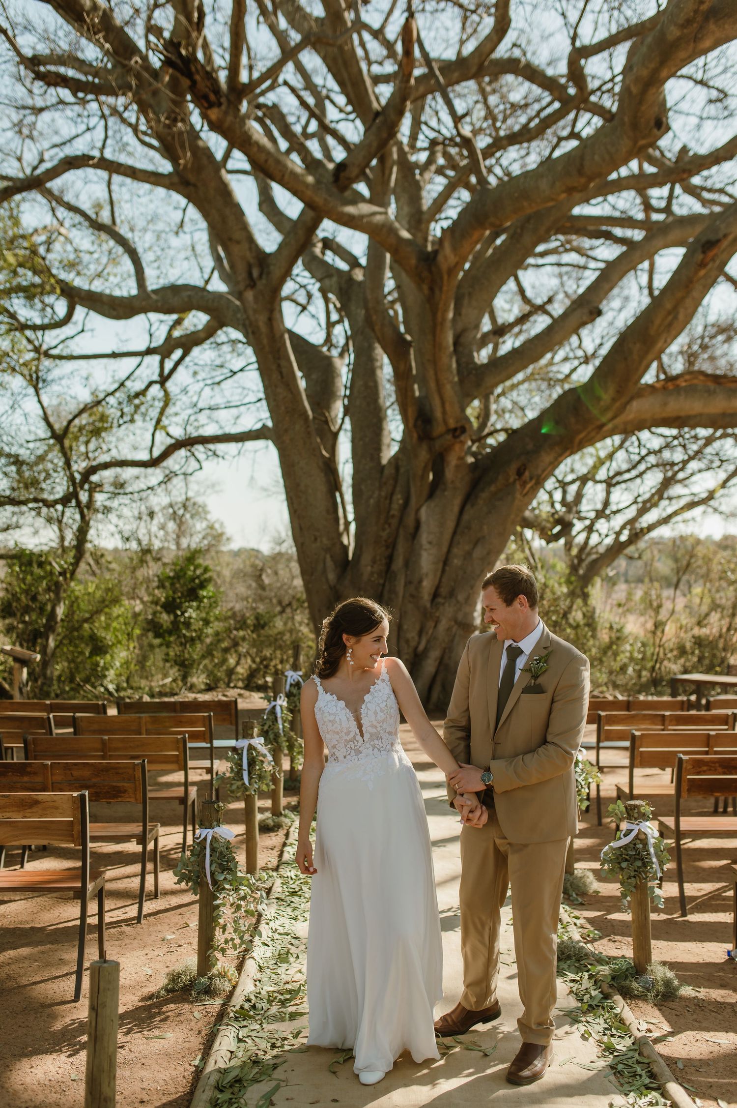 Couple shares intimate moments under large tree branches at outdoor wedding ceremony venue.