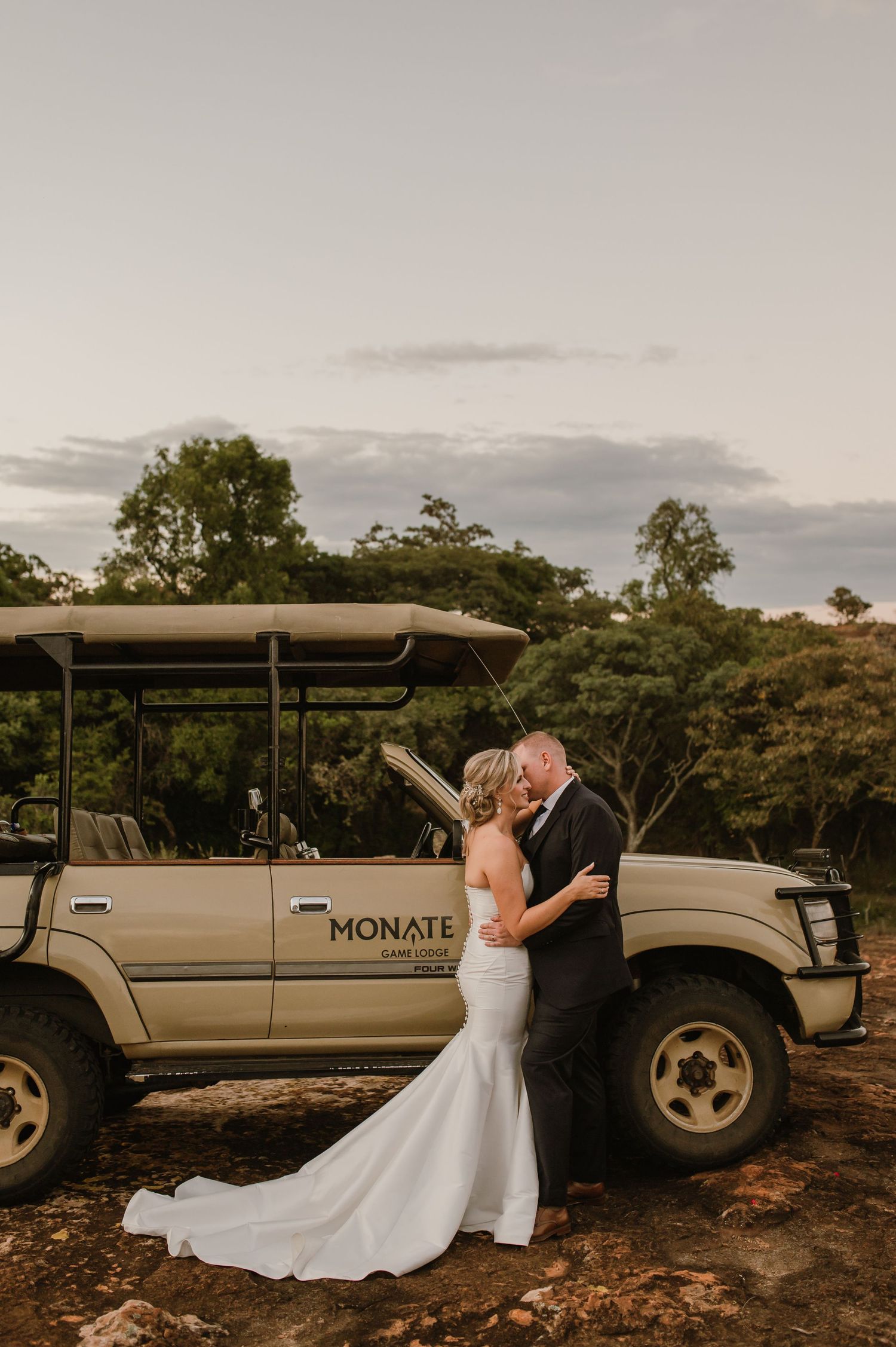 Wedding couple poses next to a safari vehicle during golden hour.