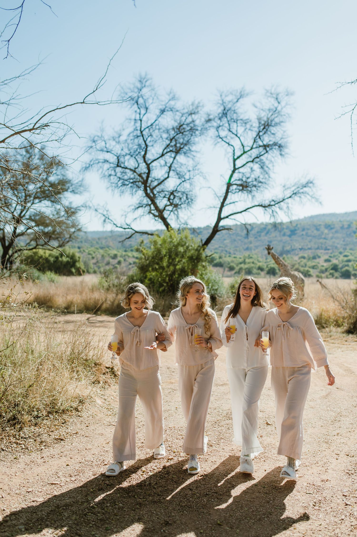 Group in matching white outfits walking and laughing together on a sunny desert path.