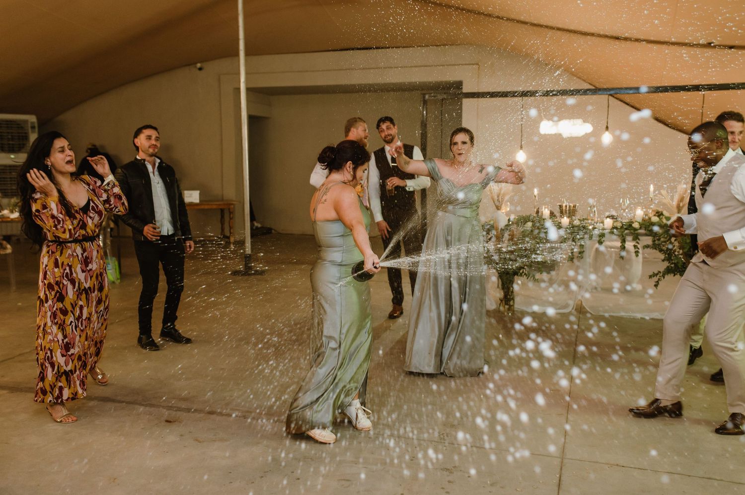 Guests dancing amid bubbles under string lights at an outdoor wedding reception.