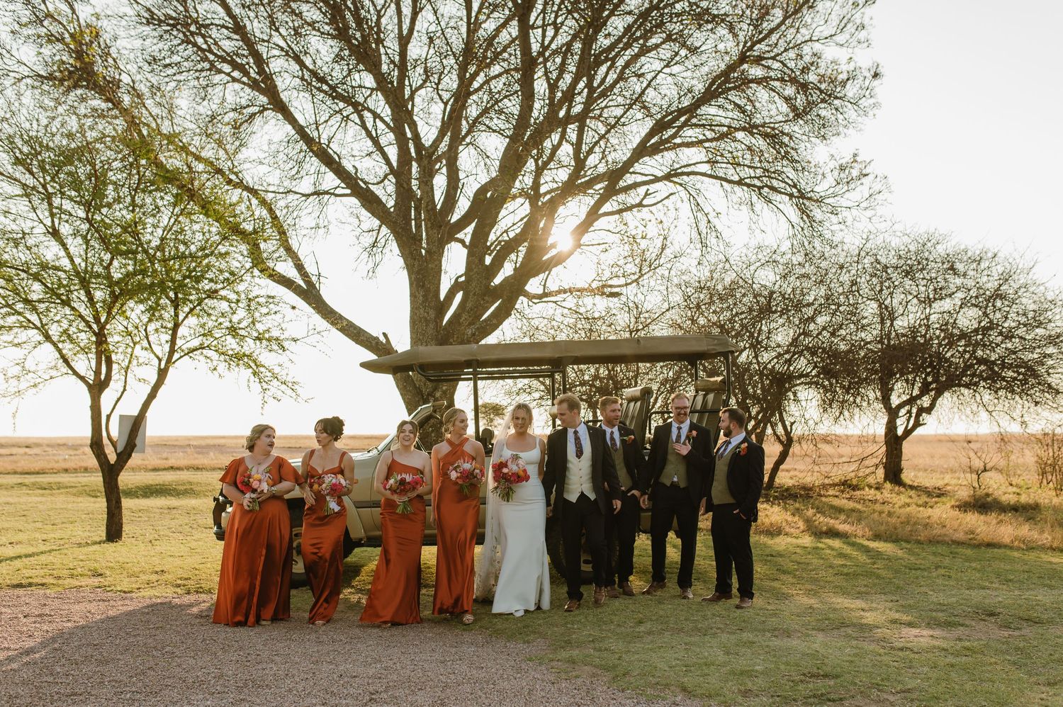 Wedding party arranged in a panoramic shot under trees at golden hour.