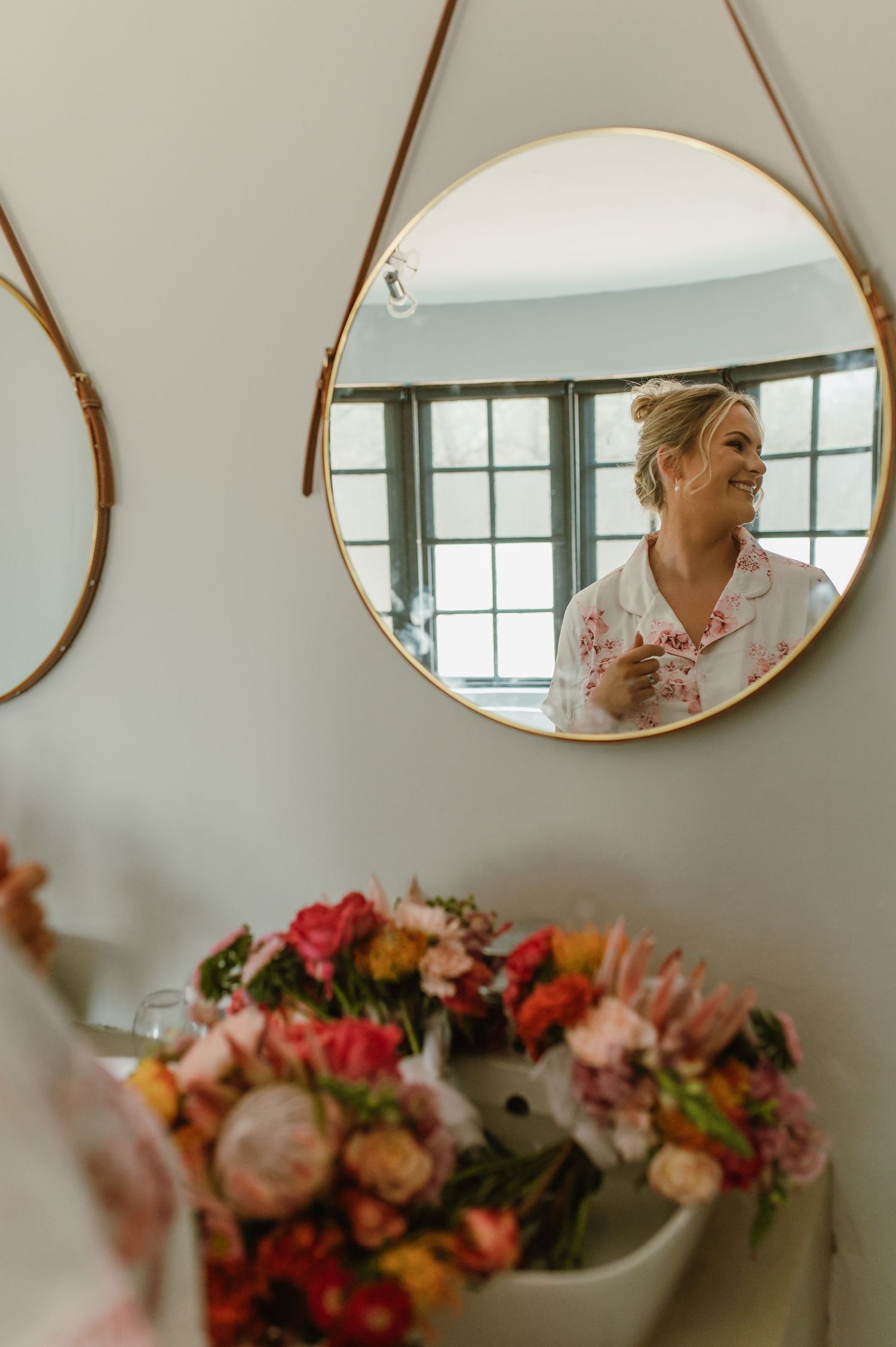 Round gold mirrors hanging on wall above colorful floral arrangements.