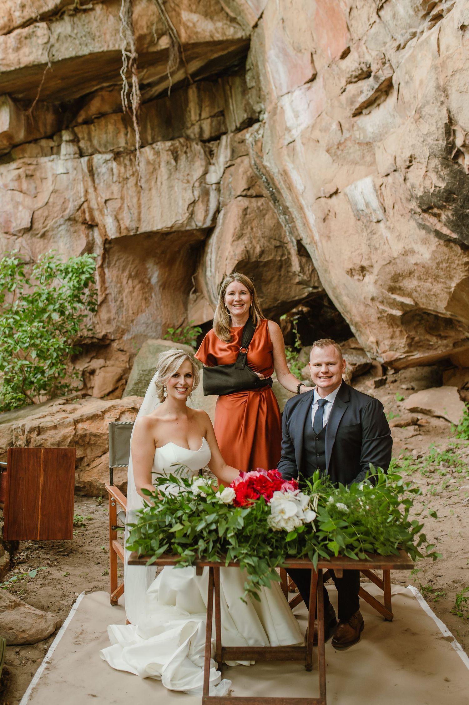 Intimate wedding ceremony with guests seated in wooden chairs against dramatic rock wall backdrop.