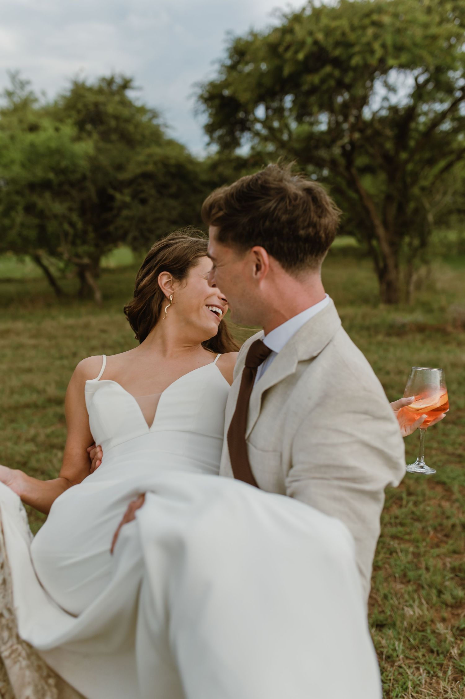 A romantic wedding moment with the groom carrying the bride while sharing drinks in an outdoor garden setting.