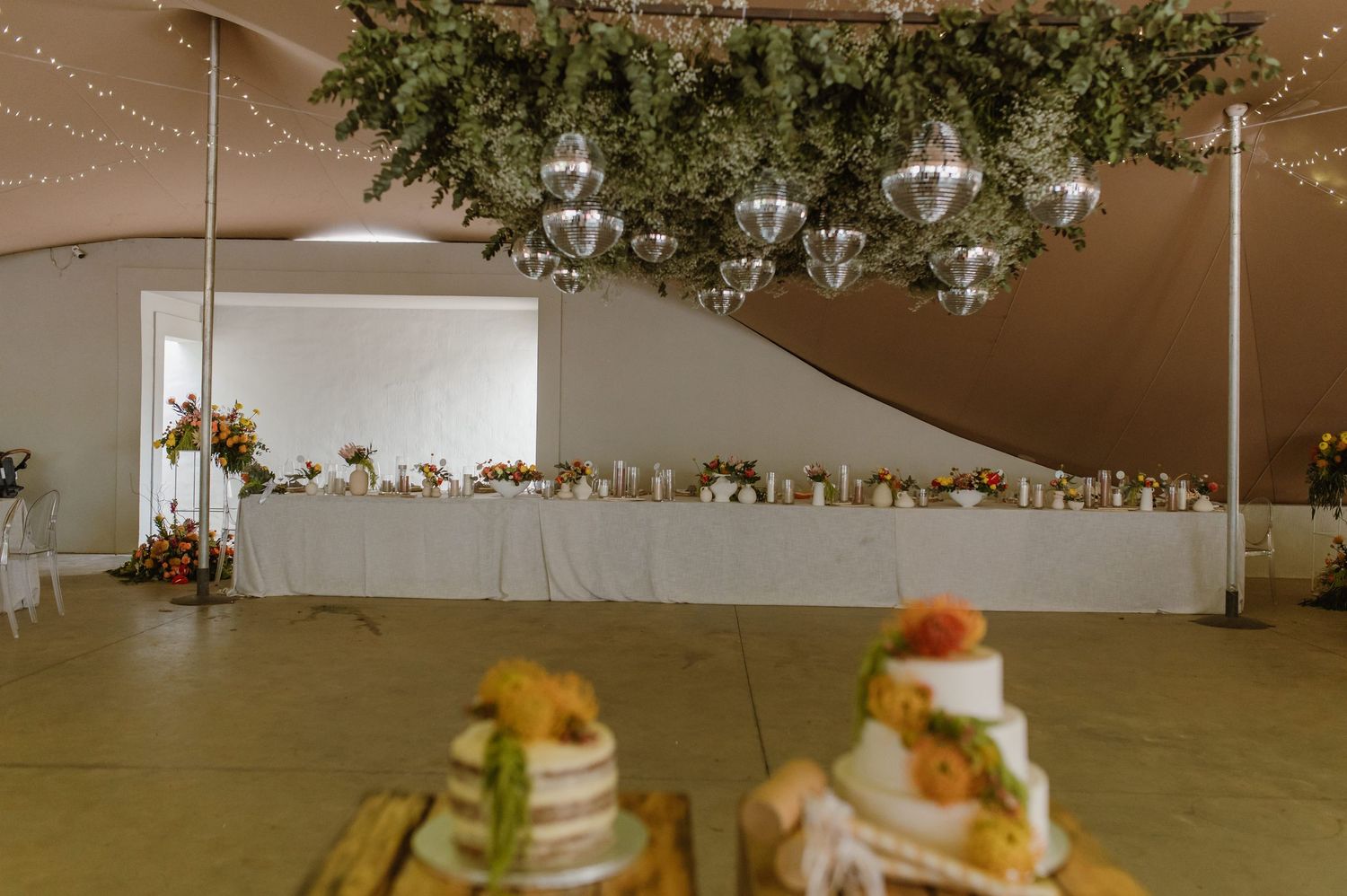 Wedding reception setup with string lights and greenery decorations overhead.