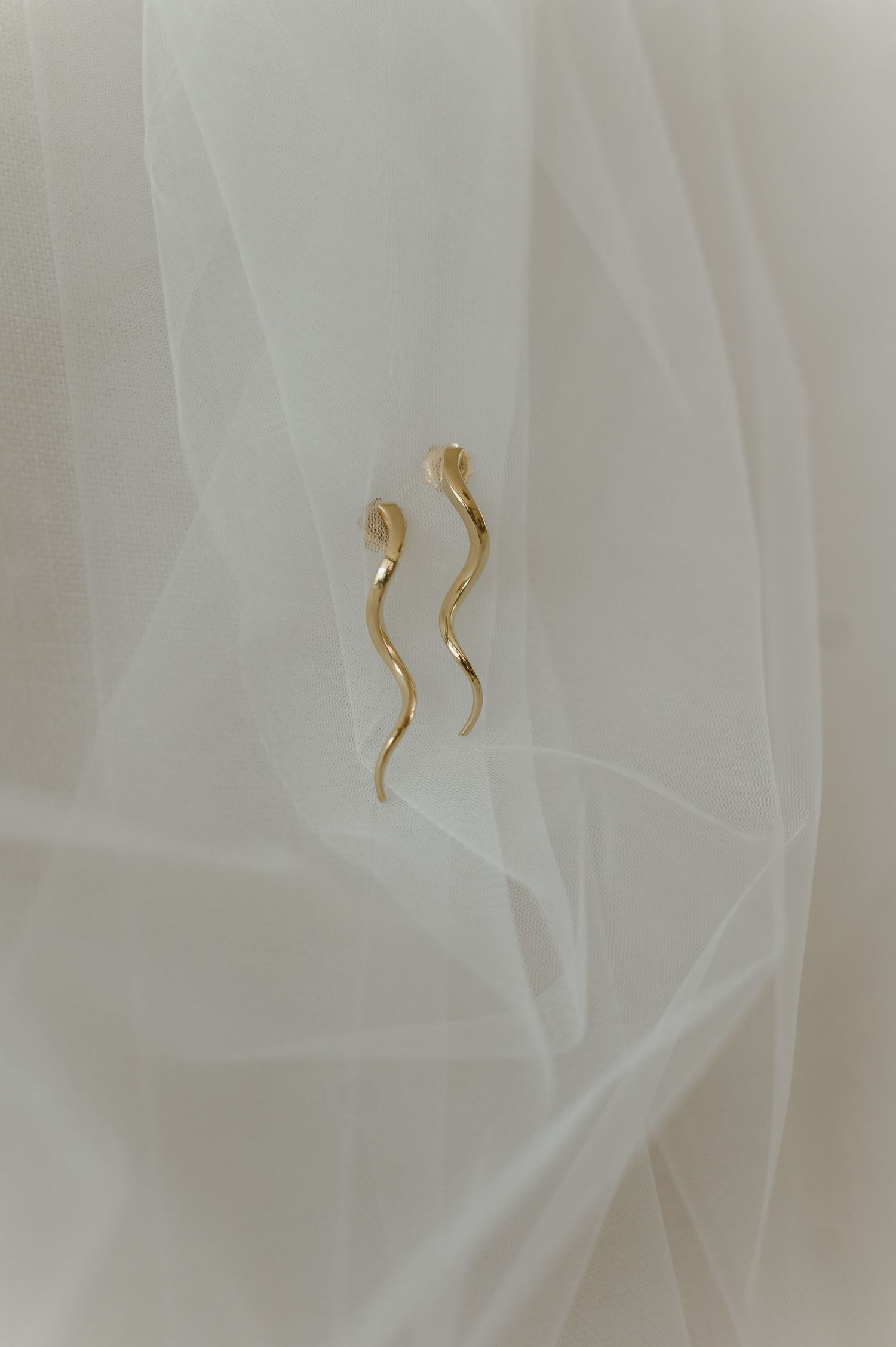 Gold earrings delicately arranged on soft white tulle fabric.