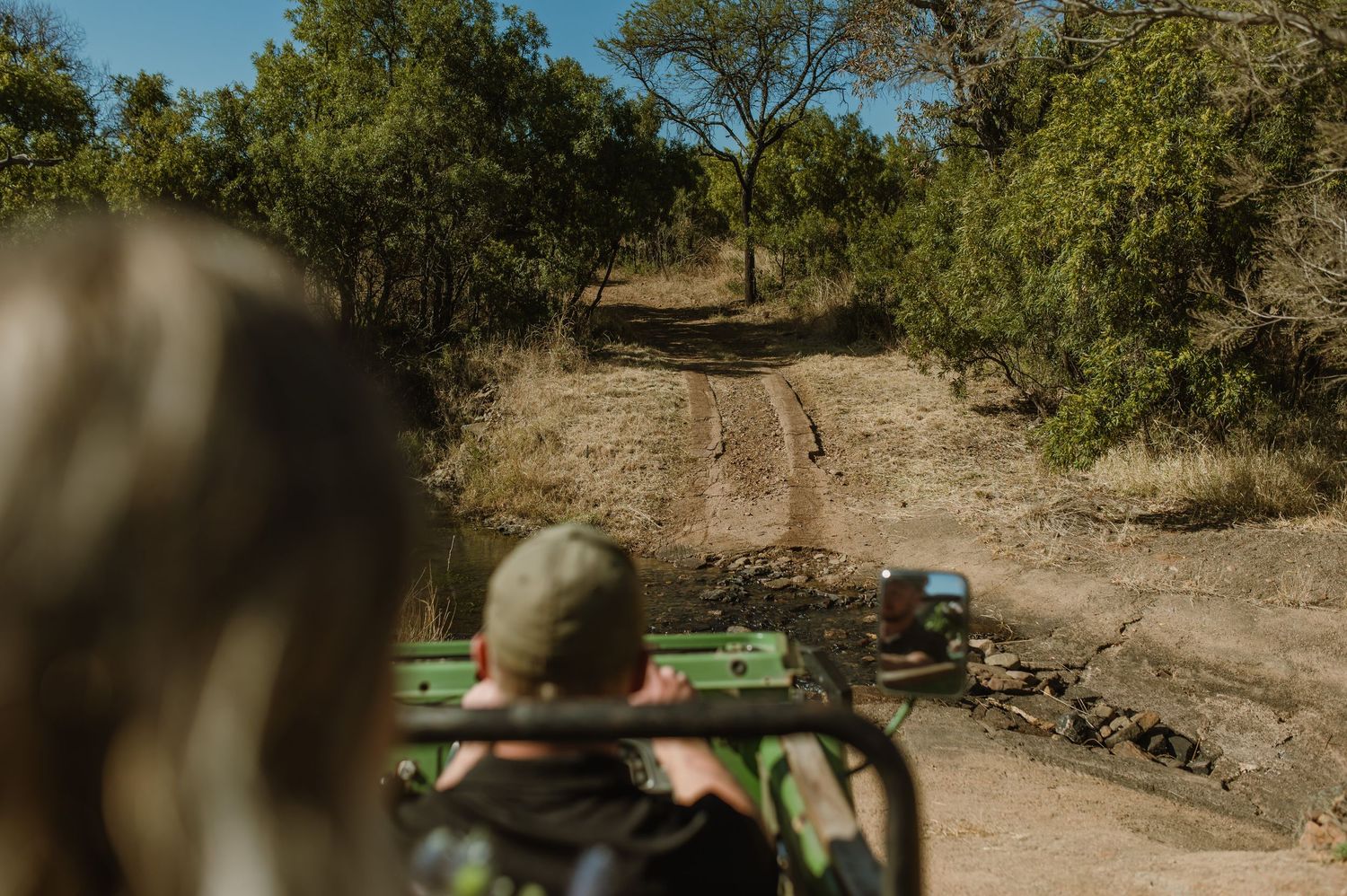 Green safari vehicle navigating through rough desert terrain surrounded by vegetation.