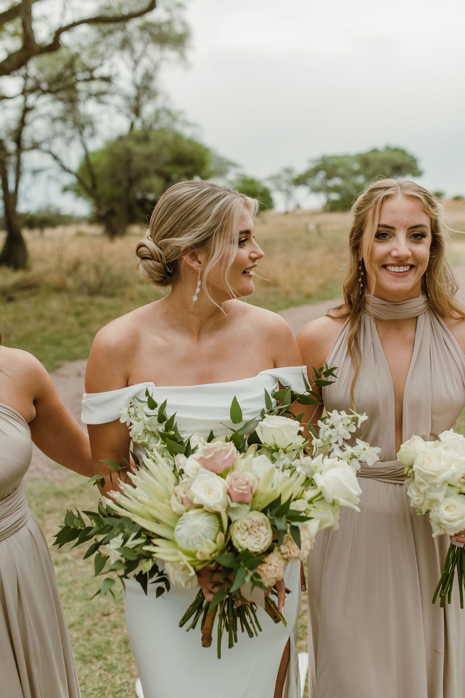 Bridal party holding elegant white and green bouquets while laughing together outdoors.