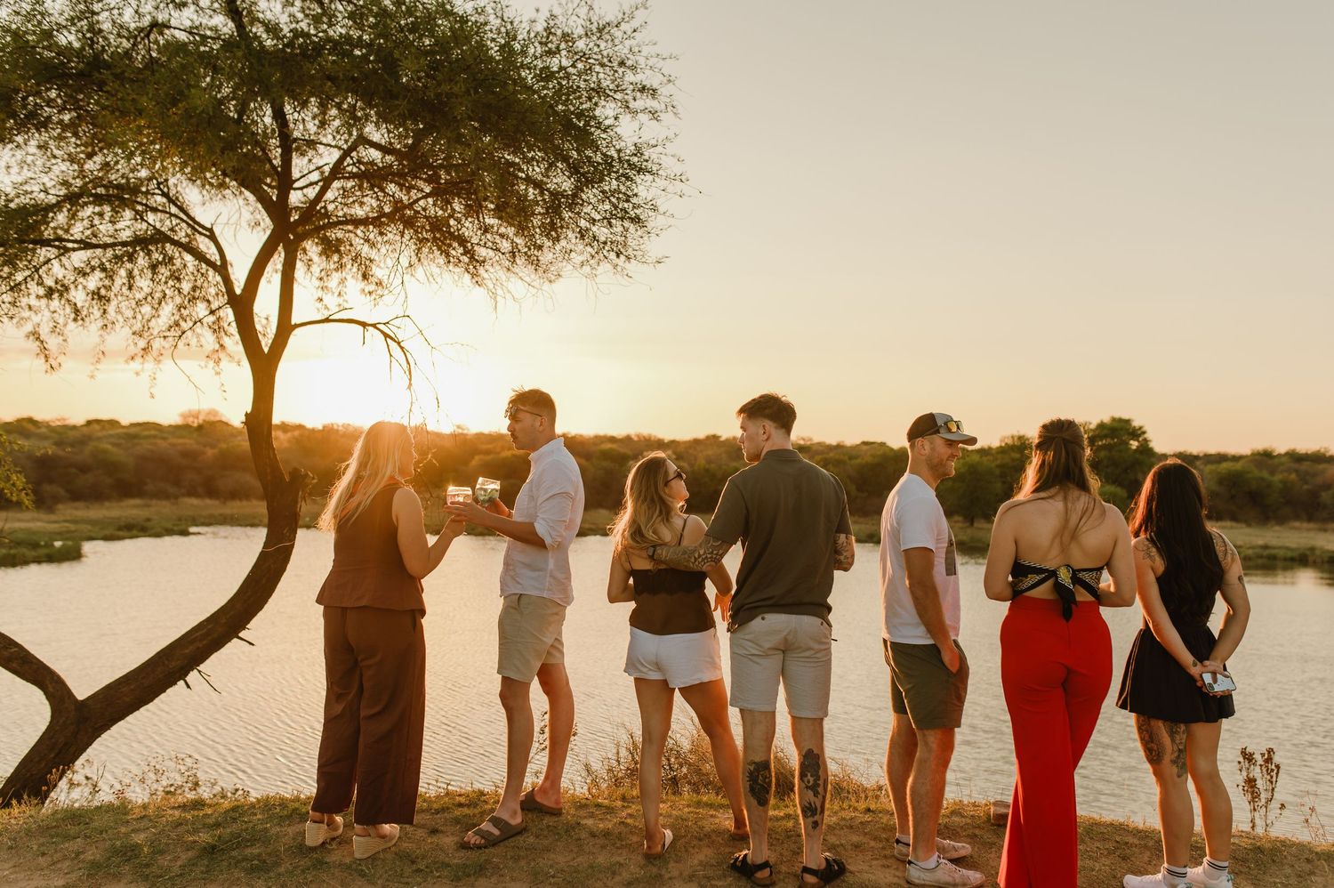 Silhouettes of people gathered along the shoreline watching the sunset over the water.