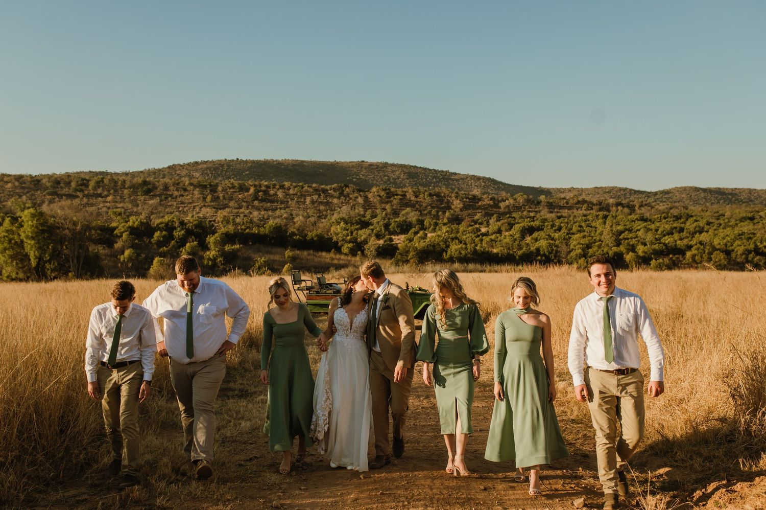 Wedding party lined up in rustic outdoor setting with mountains and golden grass.