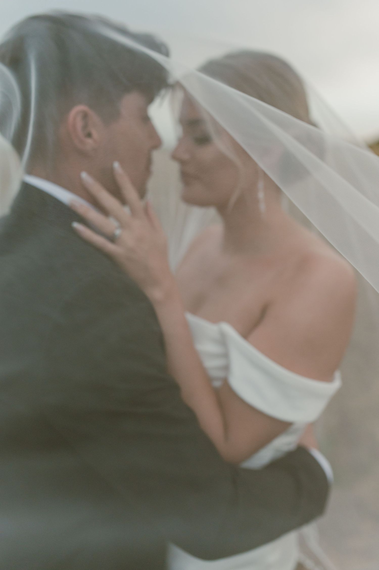 Soft focus wedding portrait shows intimate moment through flowing veil.