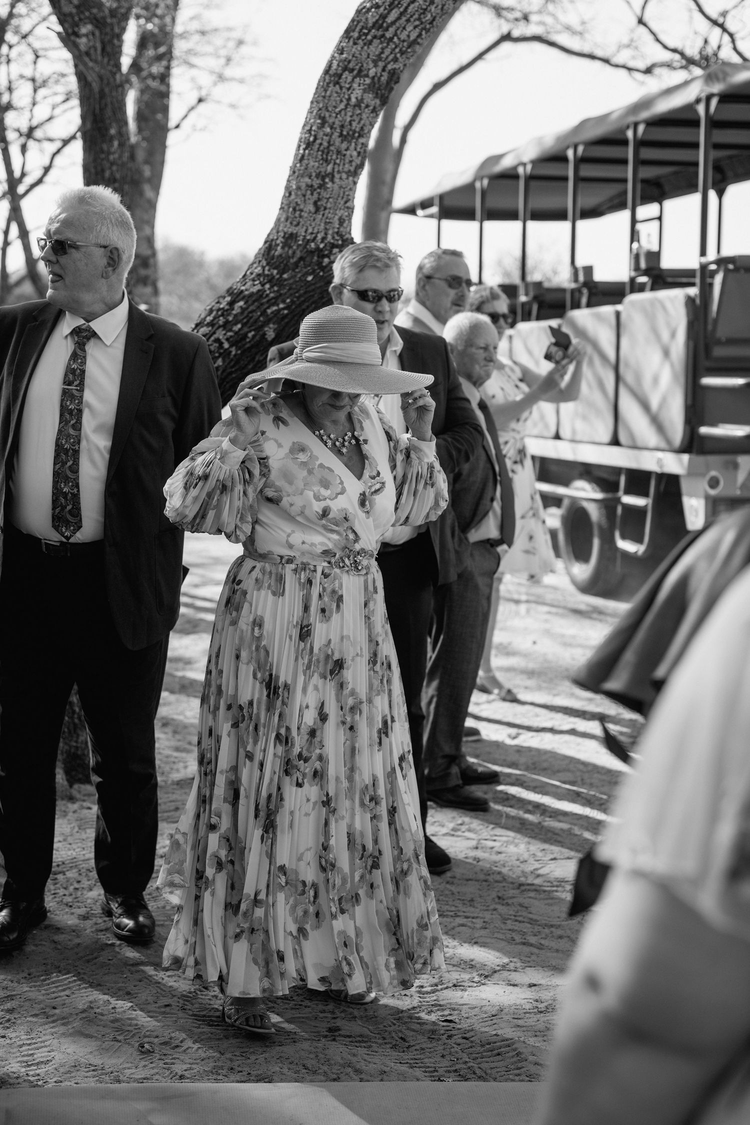 Wedding guests in formal attire dance together under trees at an outdoor venue.