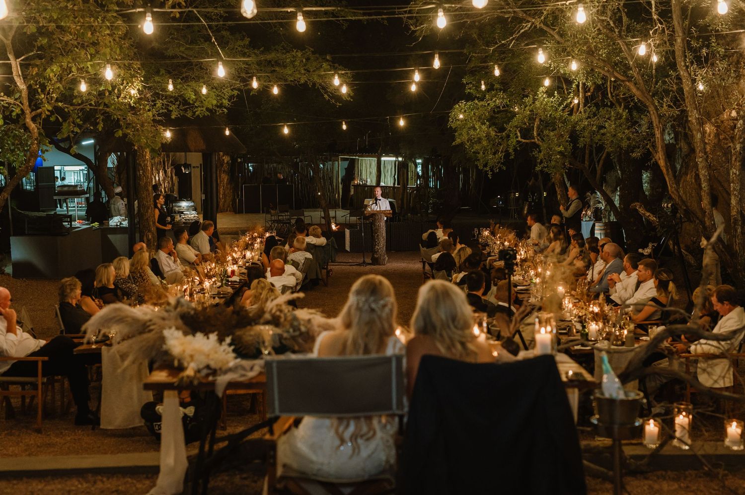 Outdoor wedding reception under string lights with long tables and elegant place settings.