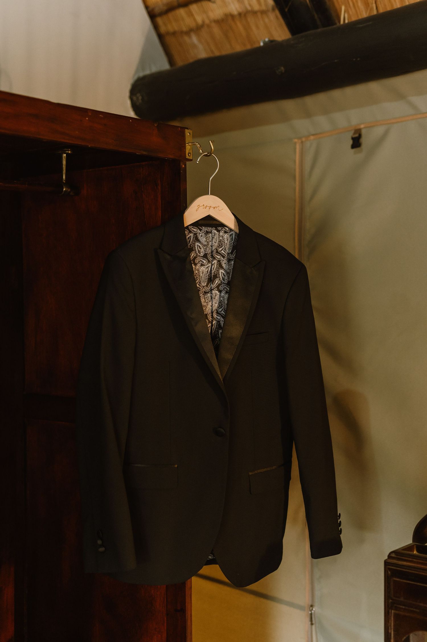 A black formal suit jacket hanging on display against a wooden wall.