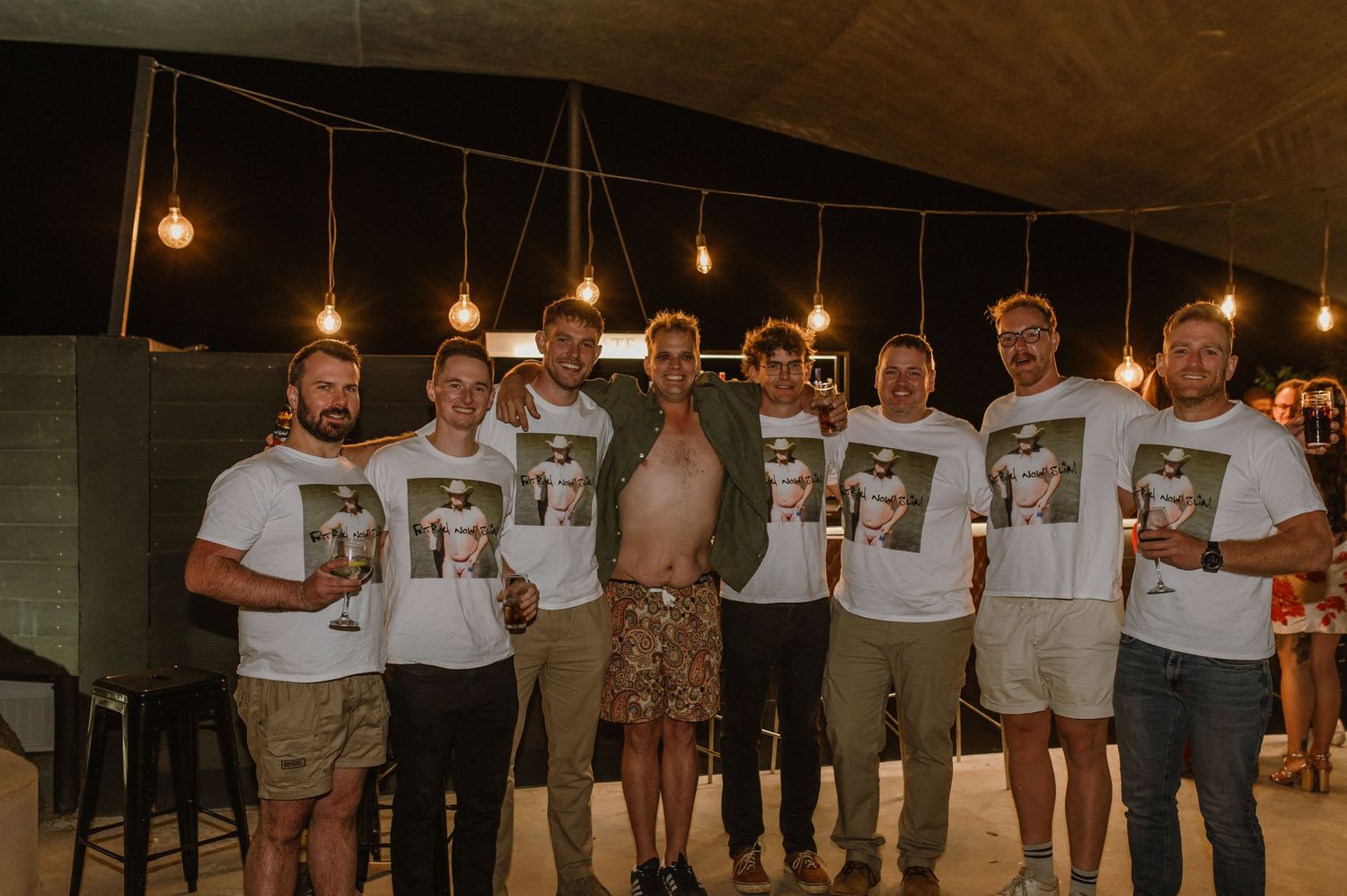 Group of people standing together in a dark room with hanging lights.
