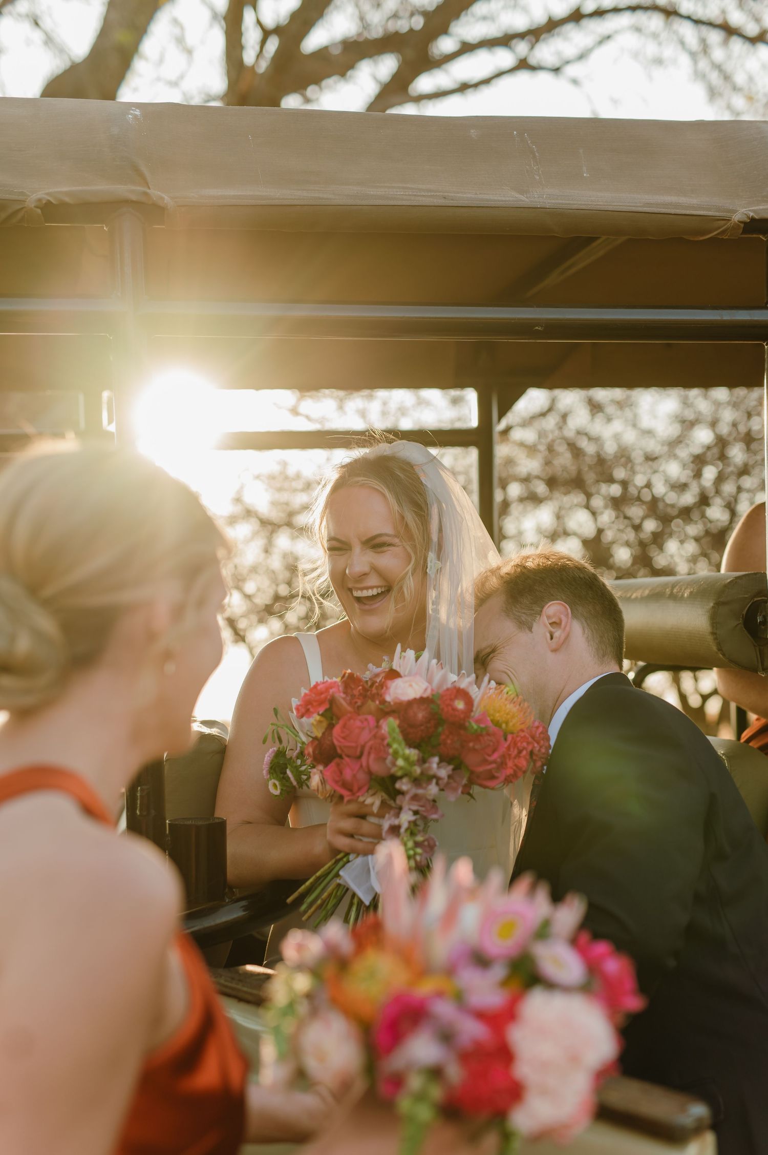 Wedding party sharing joyful moments in golden sunlight near a vehicle.
