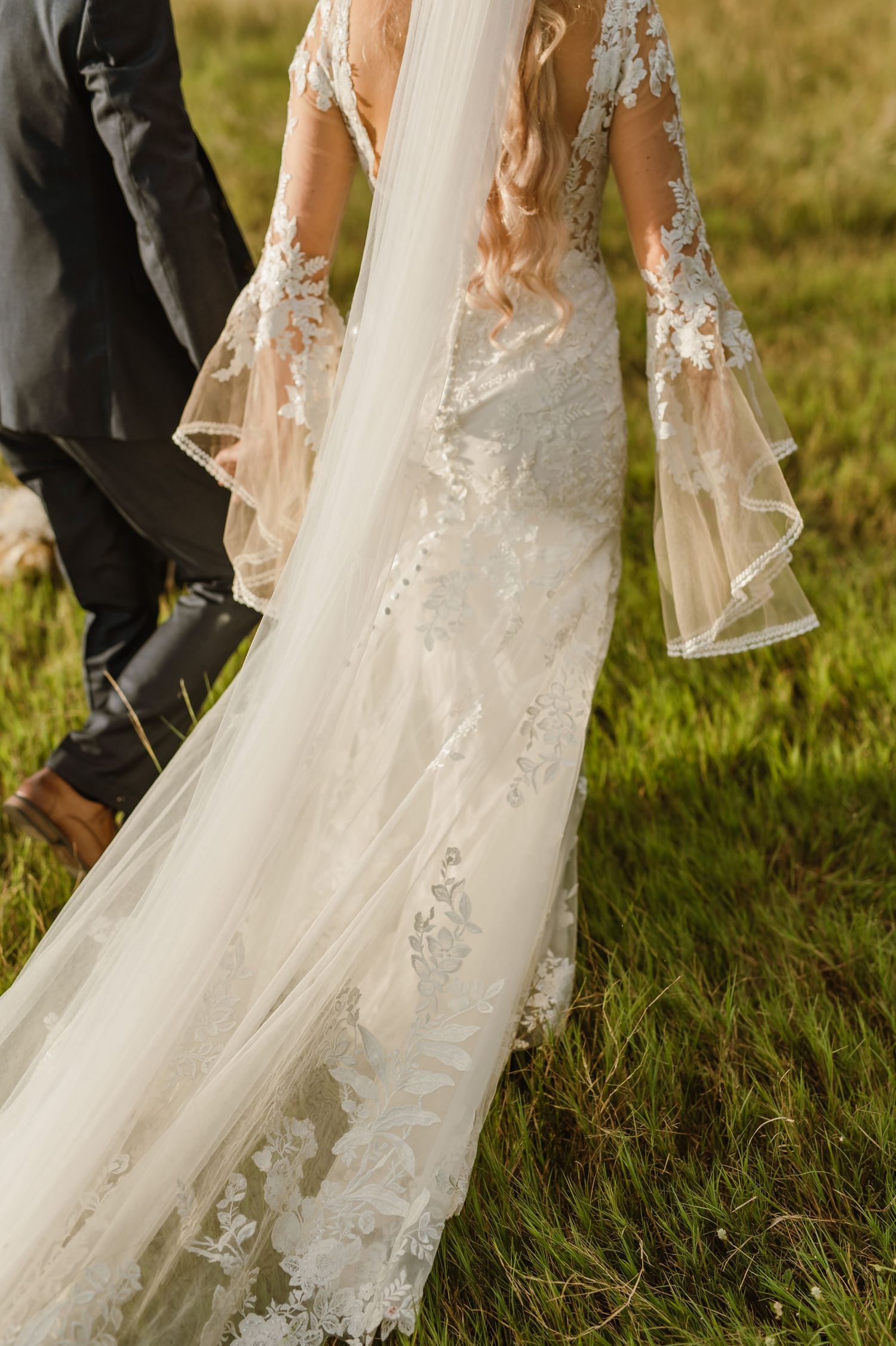 Close-up detail of a flowing white lace wedding dress train against green grass.