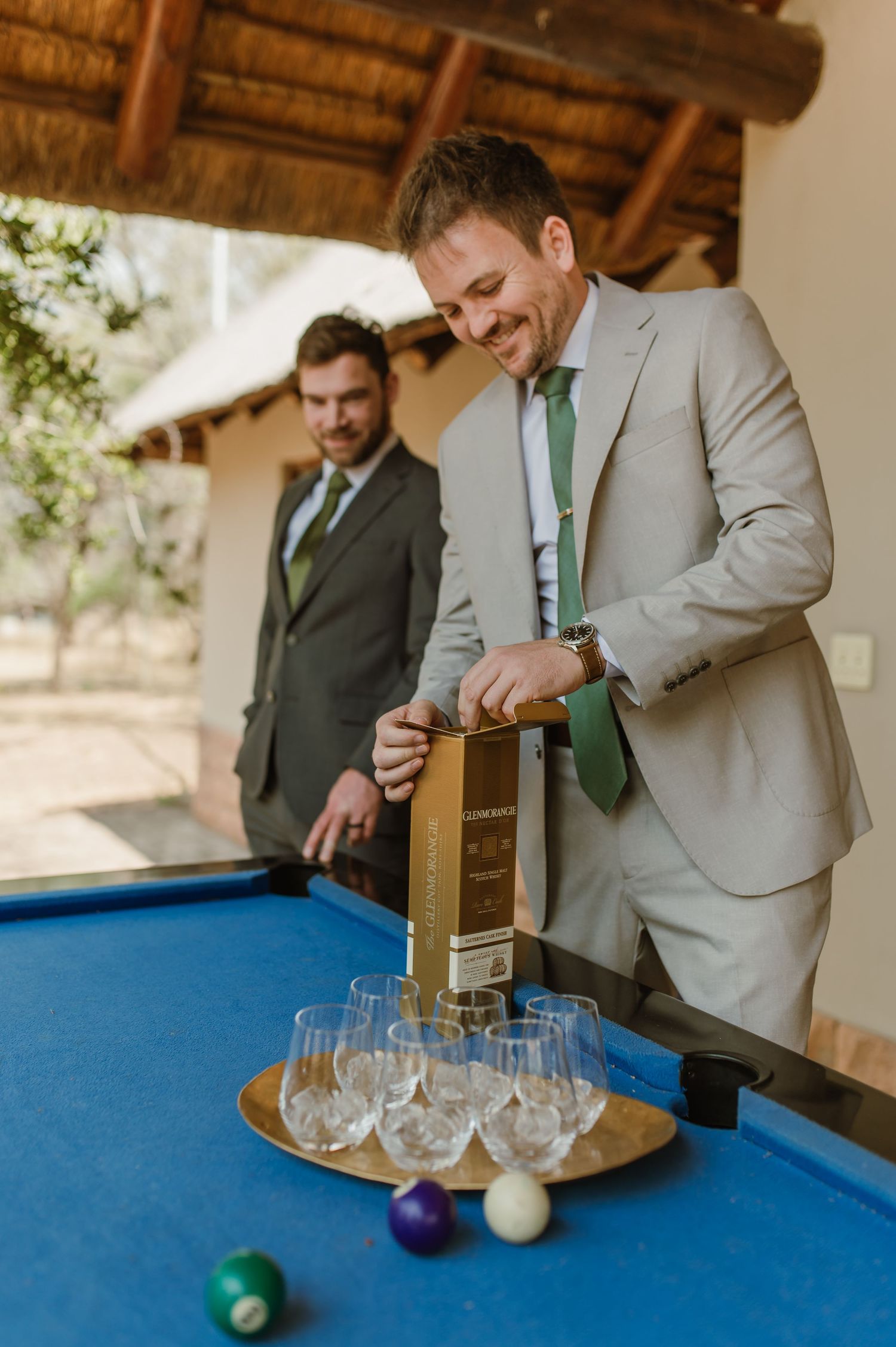 Groomsmen pouring drinks into glasses on a blue pool table with billiard balls.