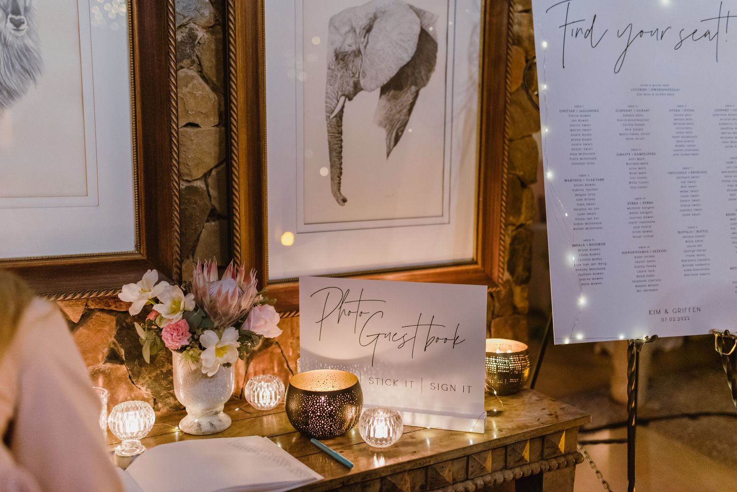 Wedding signage and seating charts displayed on rustic stone wall with ambient lighting.