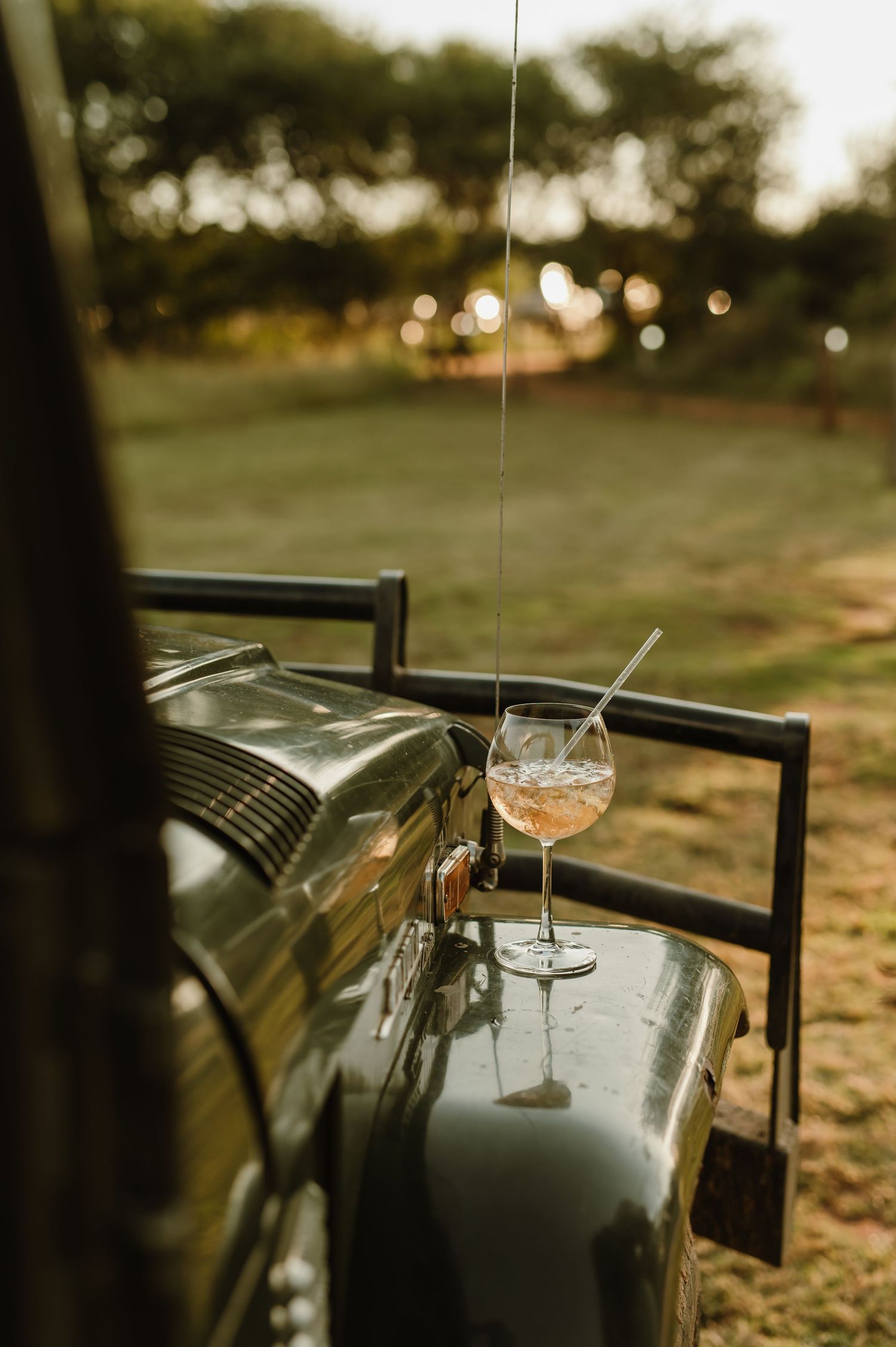 A glass of wine sits atop a vintage car hood at sunset, creating a romantic outdoor ambiance.