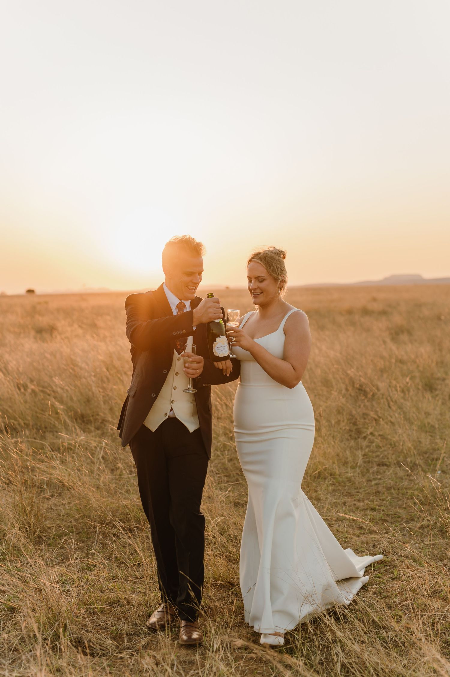 A couple dances together in a golden field at sunset during their wedding celebration.
