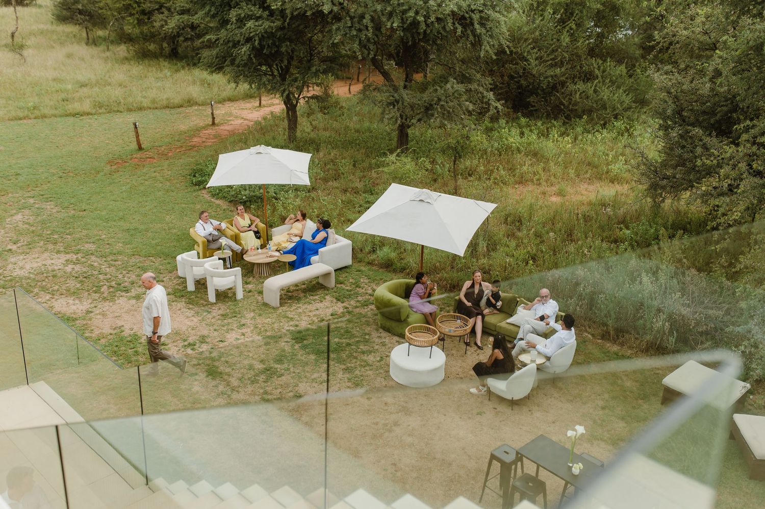 People gather under canopies for an outdoor event in a grassy area with trees in the background.