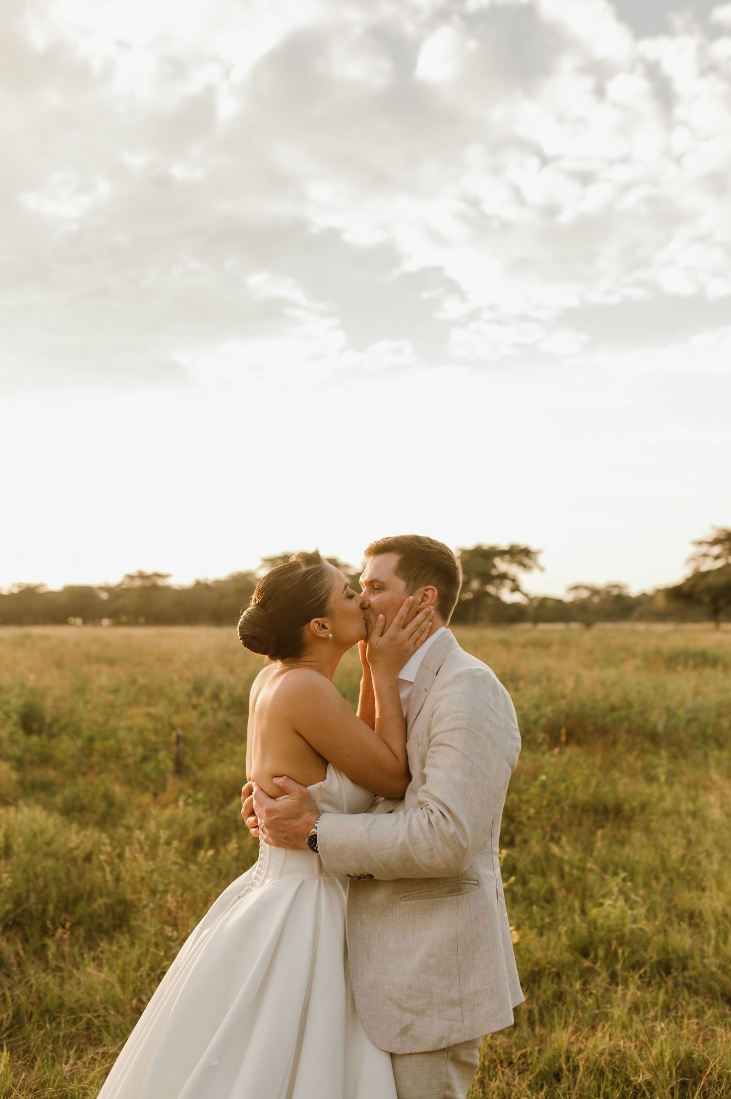 A tender wedding moment captured in a golden field during sunset with the couple sharing an intimate embrace.