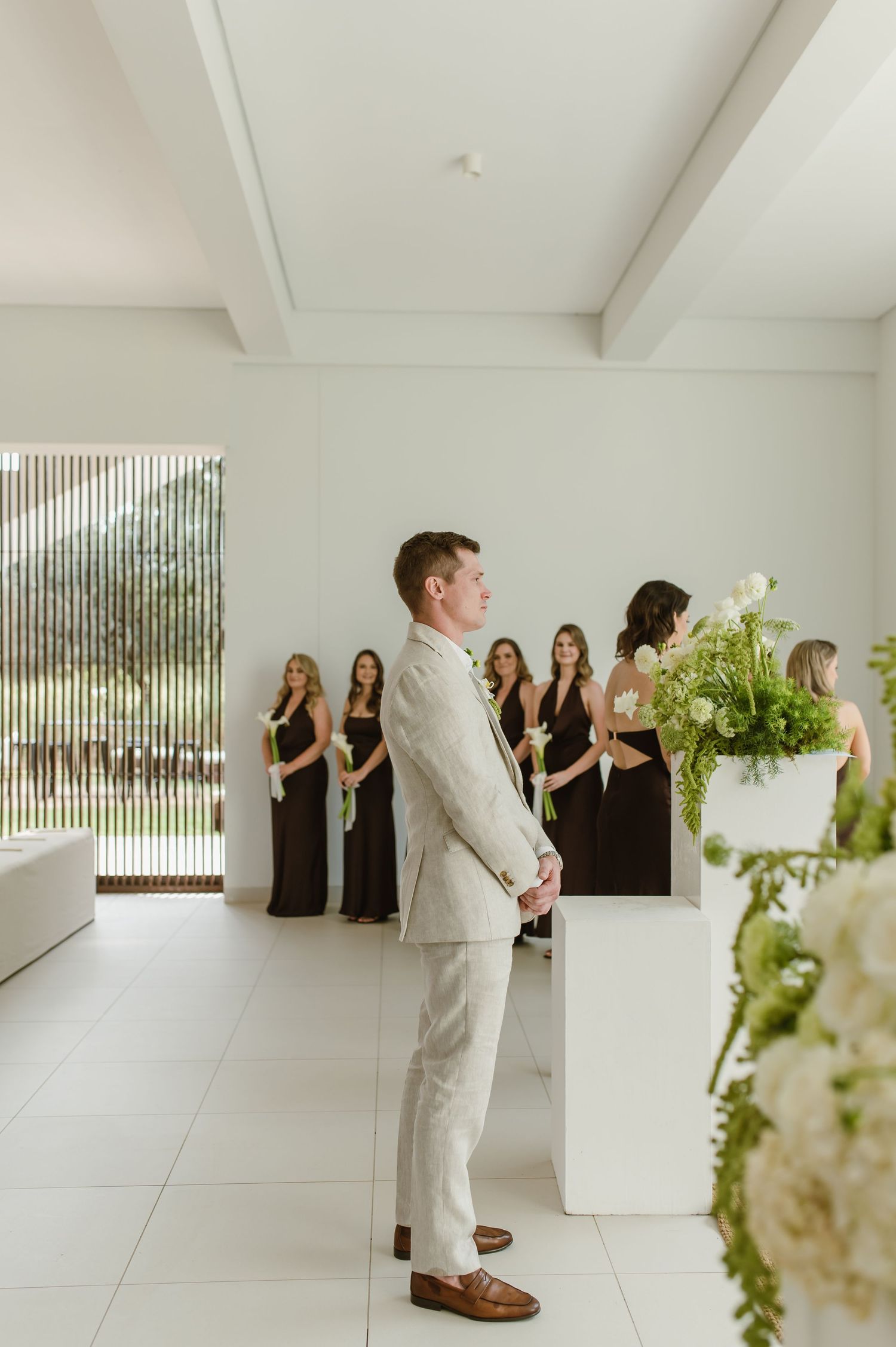 Wedding ceremony in a modern white room with floor-to-ceiling windows and floral decorations.