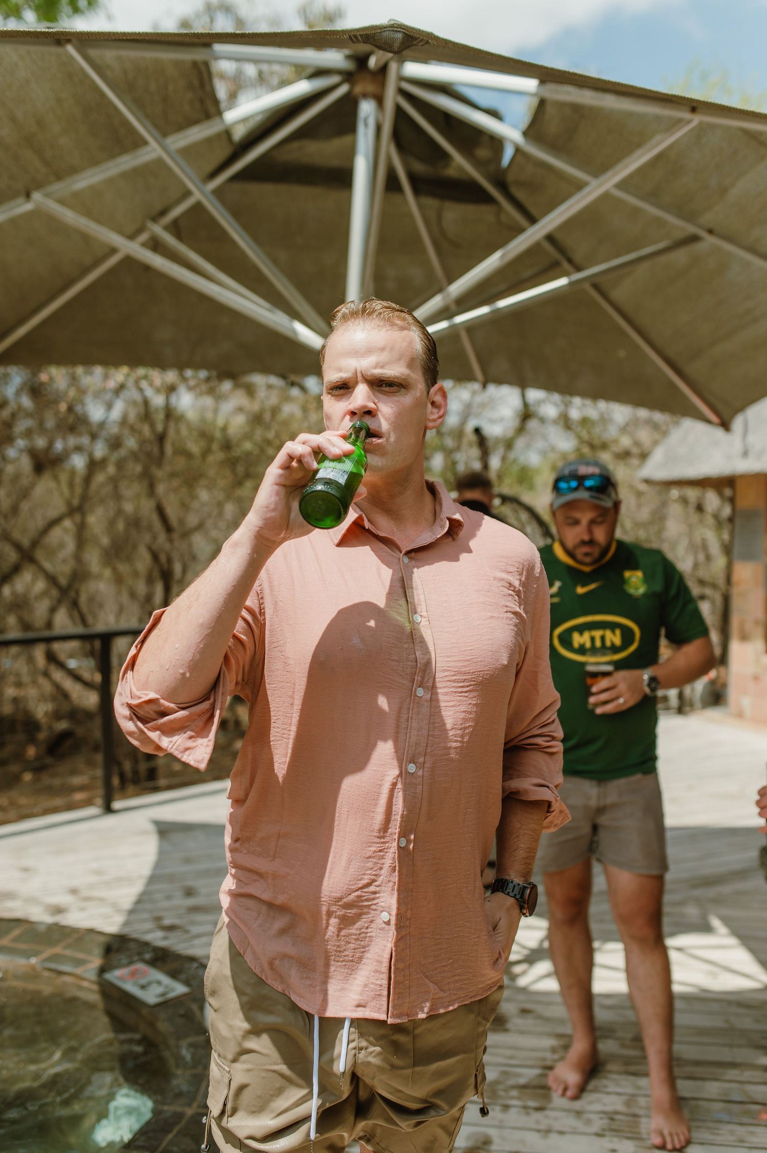Someone in a pink shirt standing under a covered outdoor area on a sunny day.
