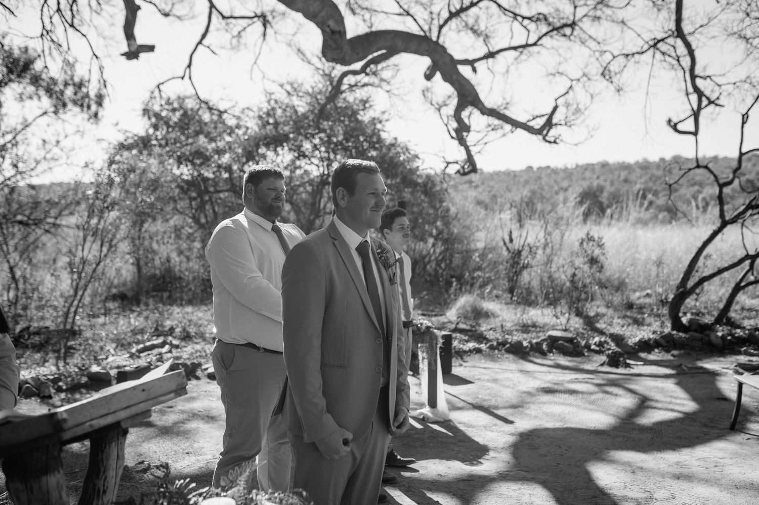 Wedding party members in formal attire walking through a desert landscape setting.