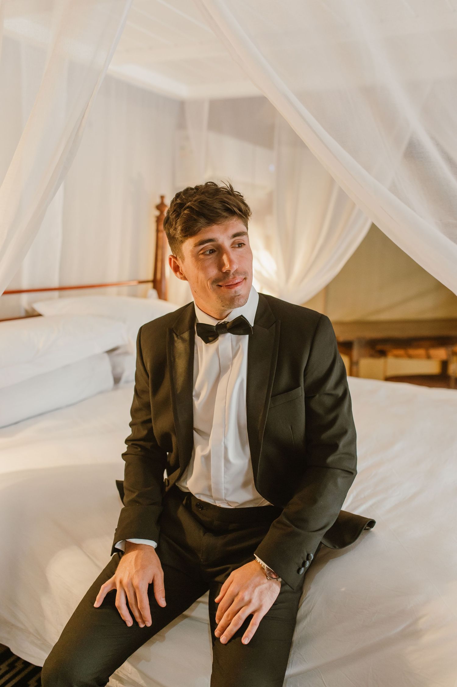Relaxed portrait on a white canopy bed showing classic black tie formal wear.
