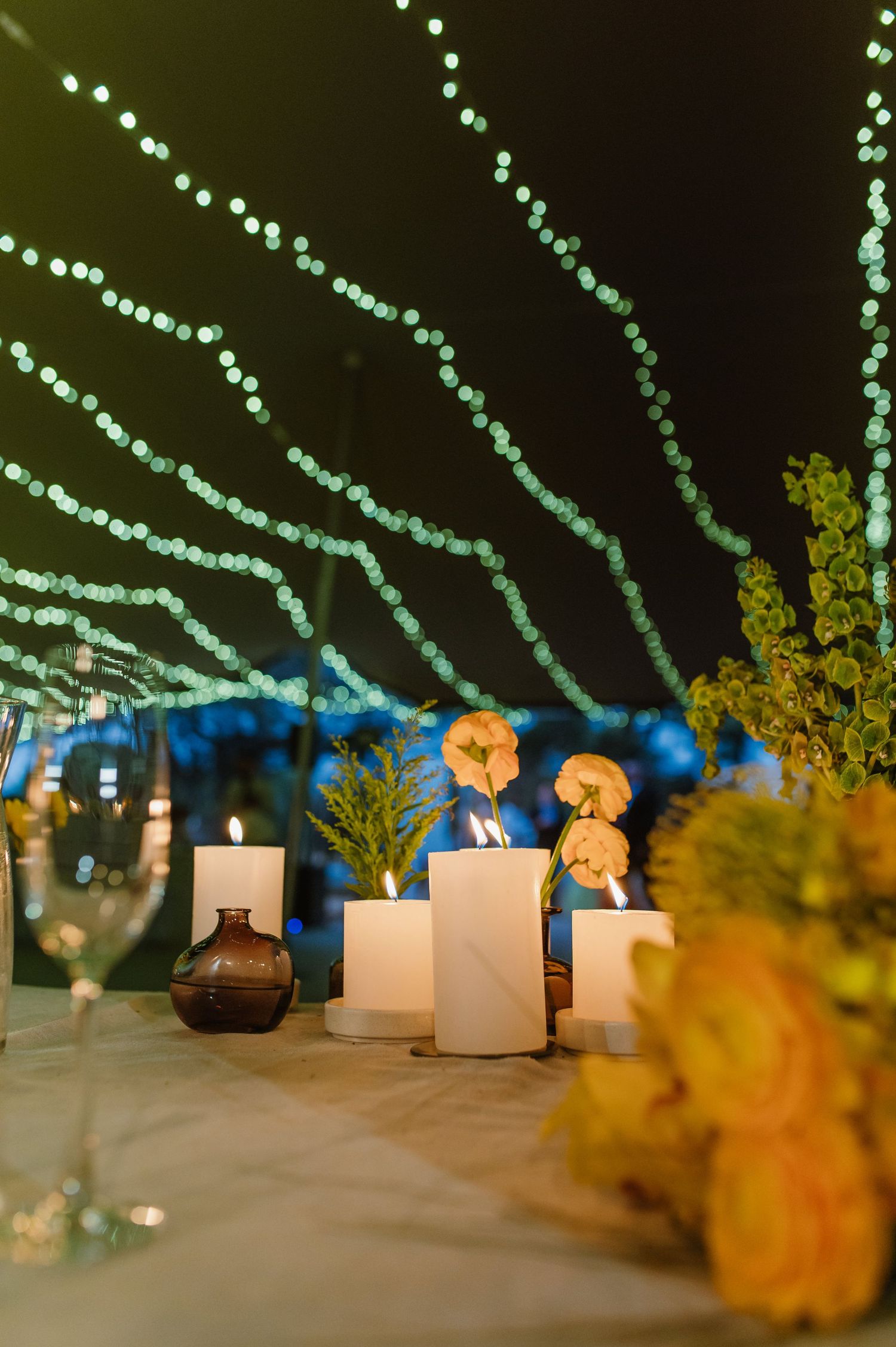 Elegant wedding reception table with candles and orange floral centerpieces under string lights.
